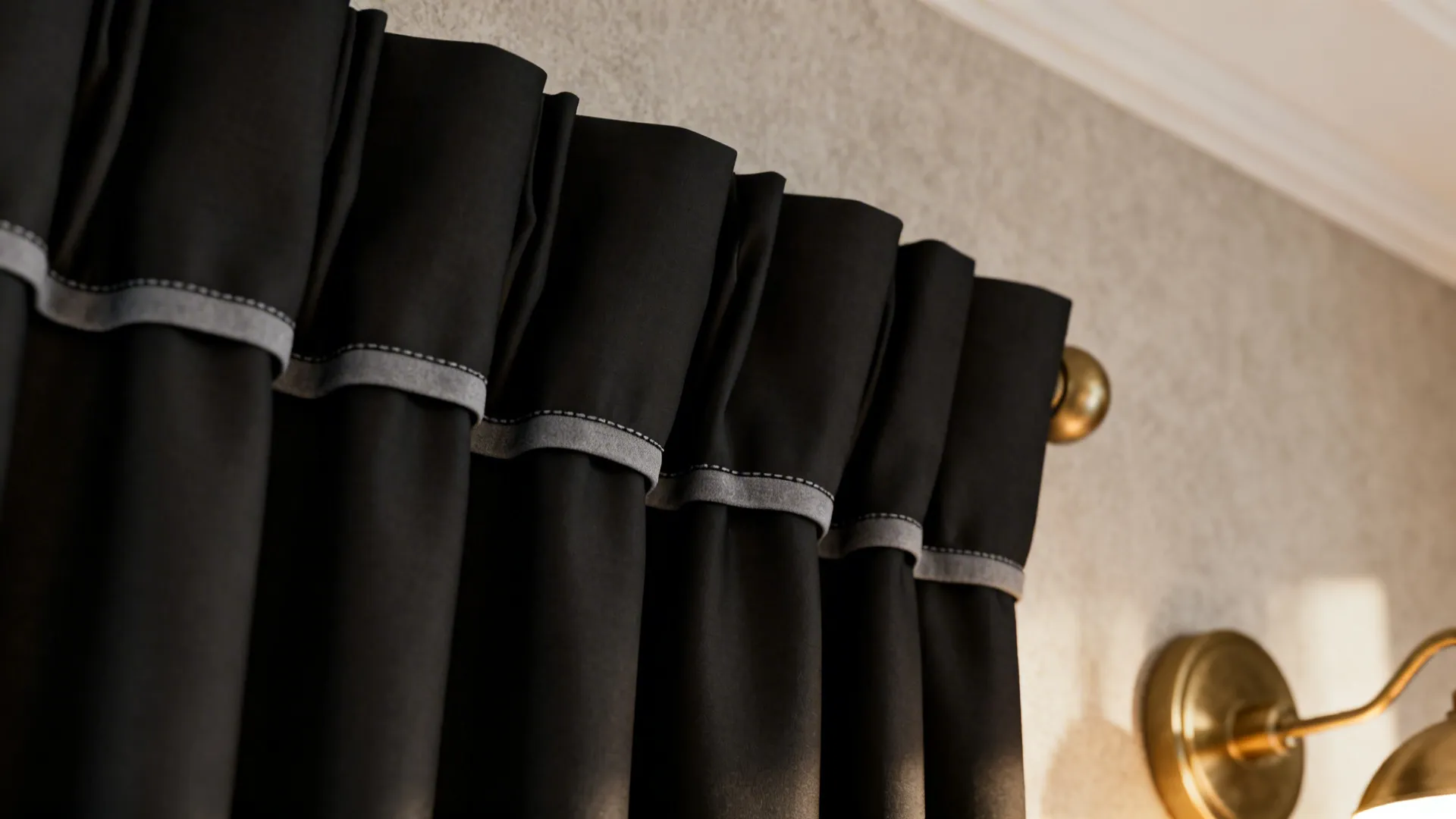 Close up of black curtains with grey trim hanging on rod near gold wall light