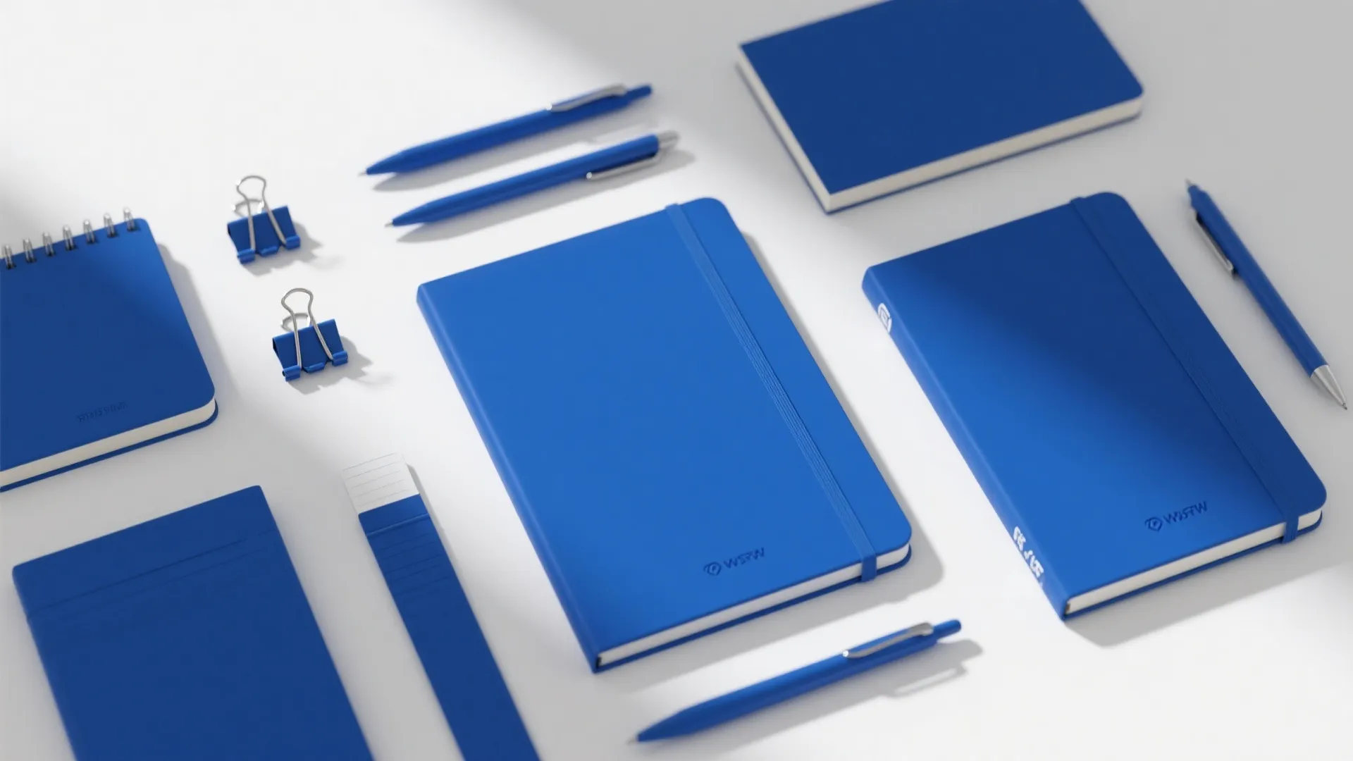 Collection of blue notebooks with pens and paper clips neatly arranged on a white surface