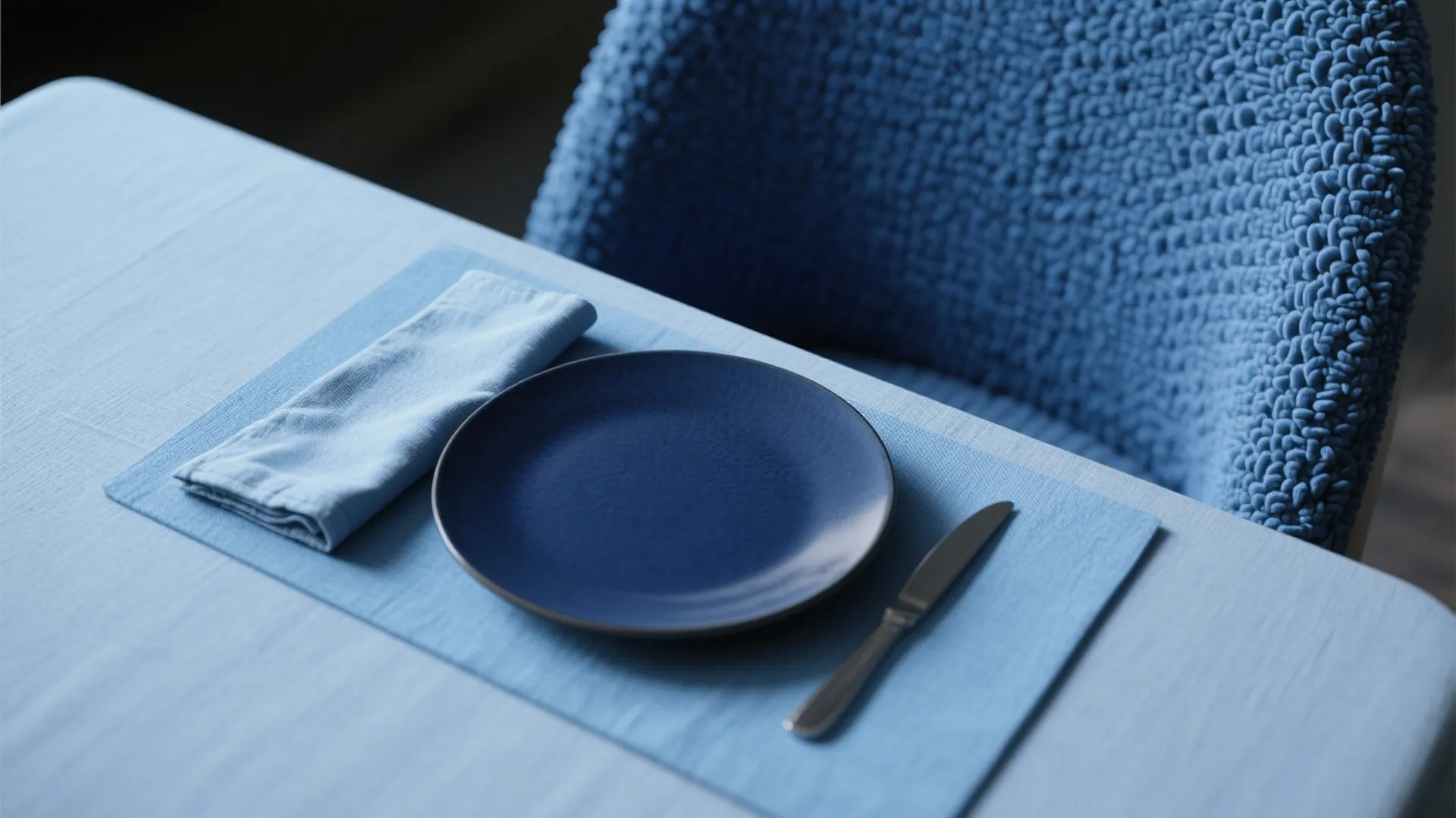 Blue dining table setup with a dark blue plate and napkin on a light blue tablecloth