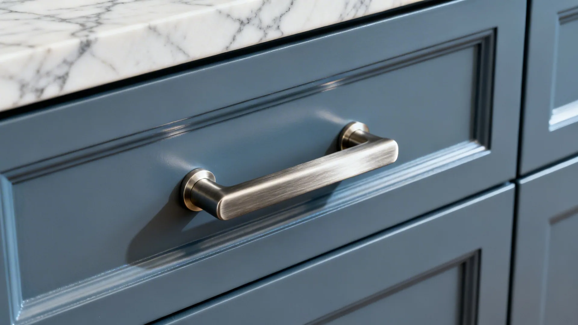 Macro of smoky blue-grey cabinet with brushed nickel pull against marble.