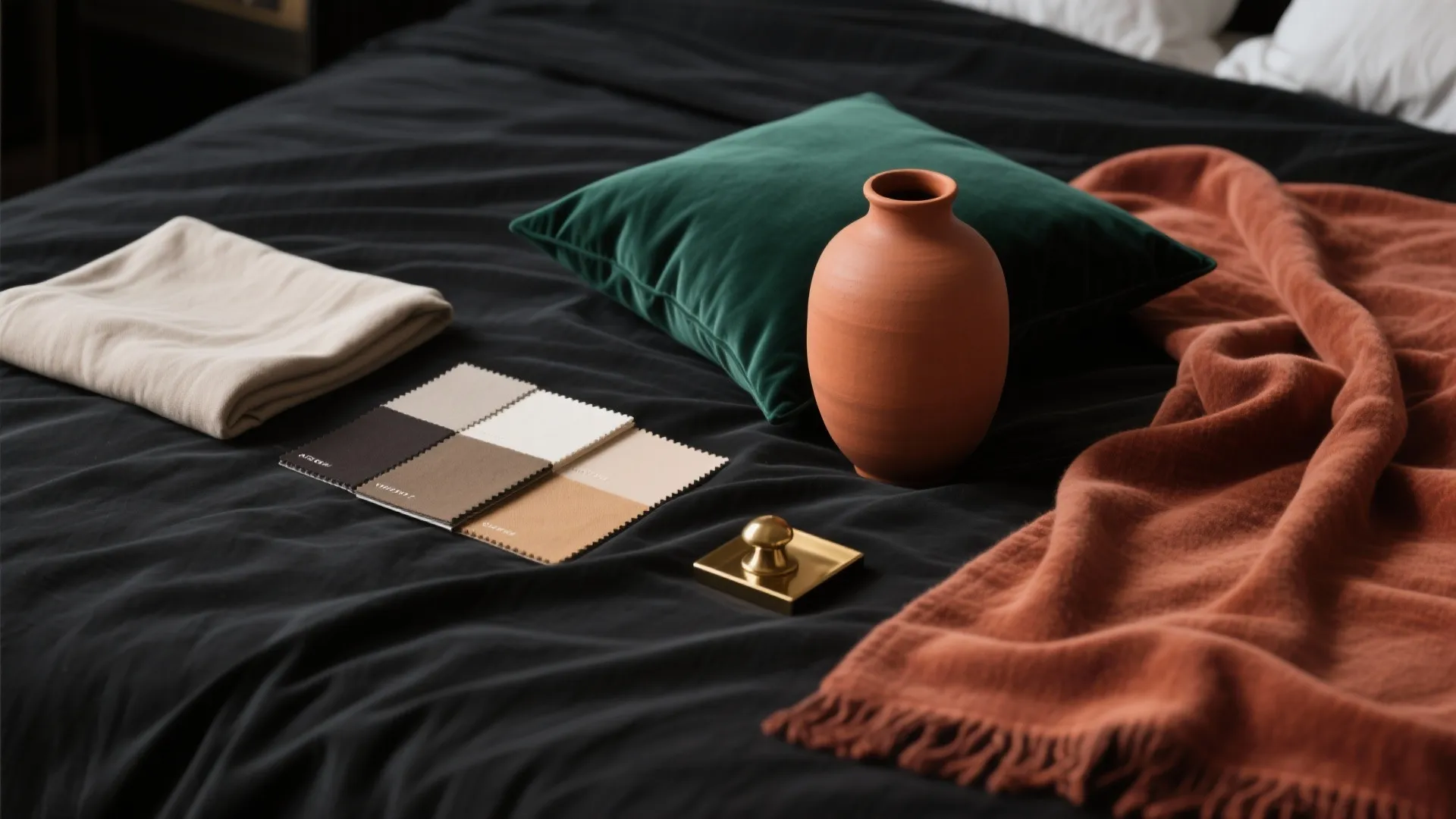 Dark bed sheets with green pillow orange vase fabric samples and a brown blanket layout