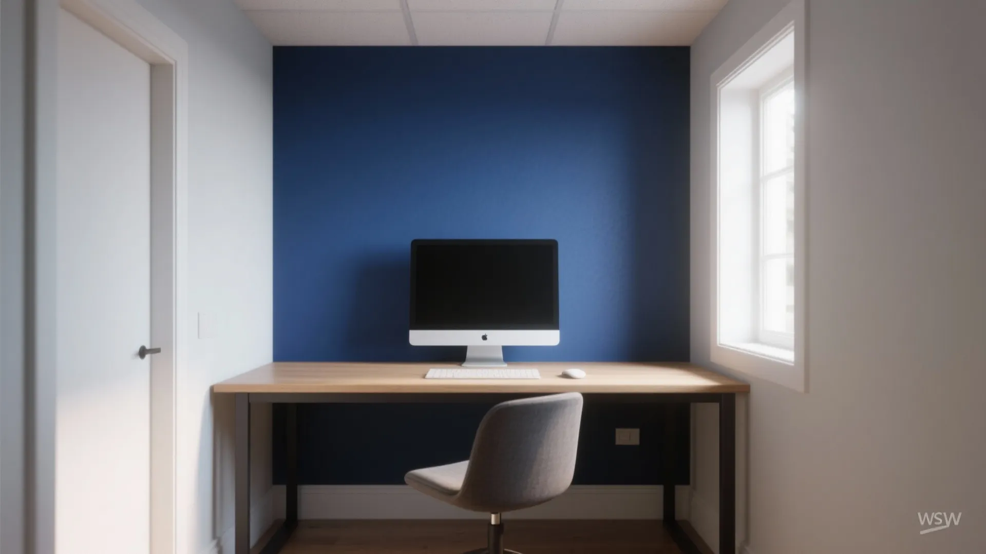 Minimalist study area with bold blue accent wall wooden desk computer and grey chair by window