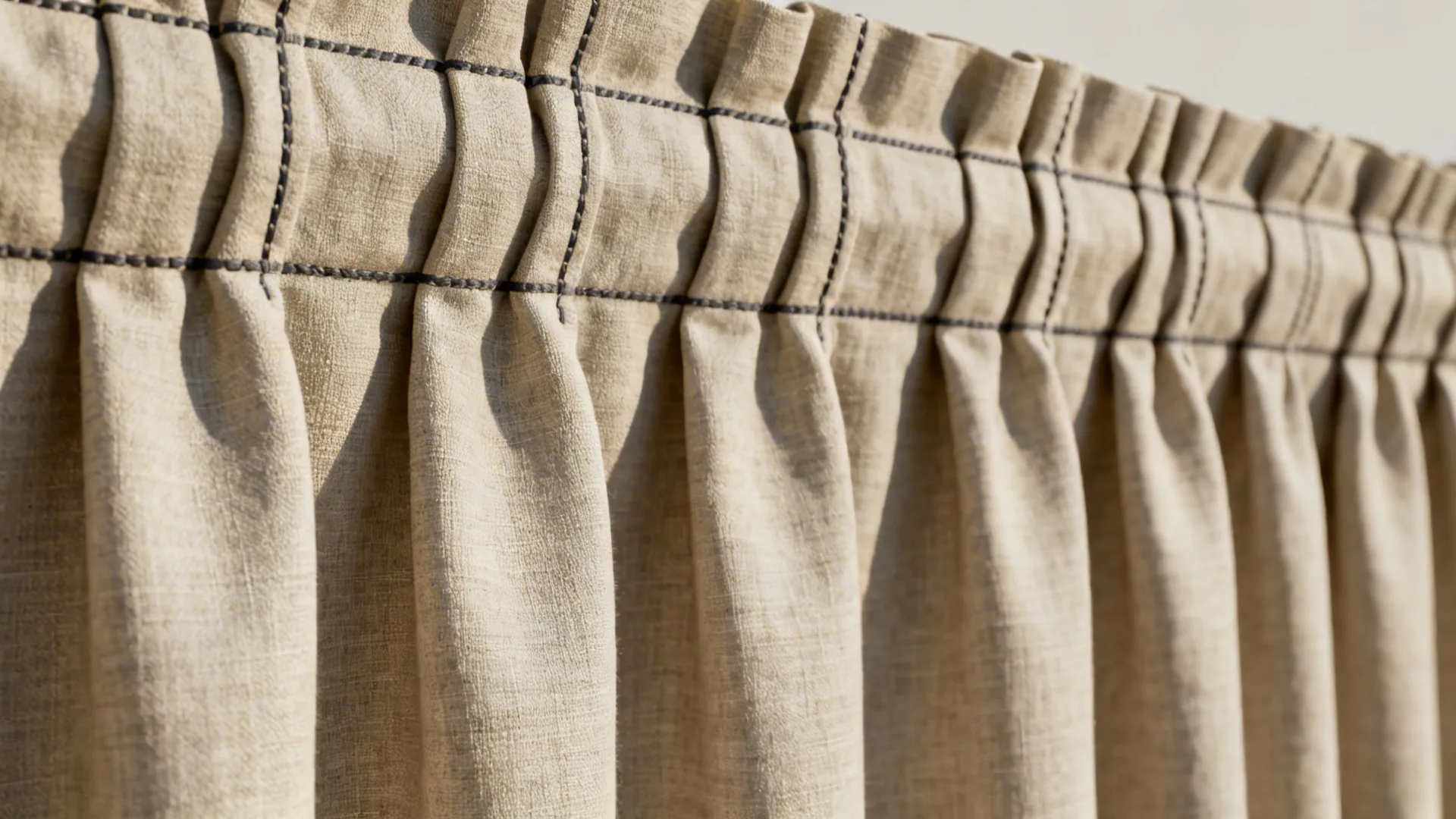 Detailed close up of beige fabric curtain showing box pleats and black stitching under bright sunlight