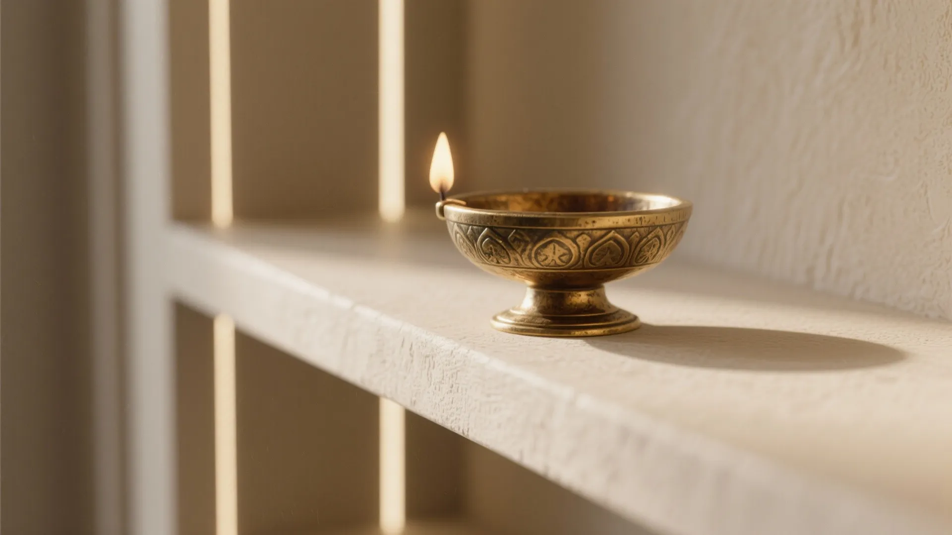 Small brass oil lamp with a lit flame sitting on a neutral stone shelf surface