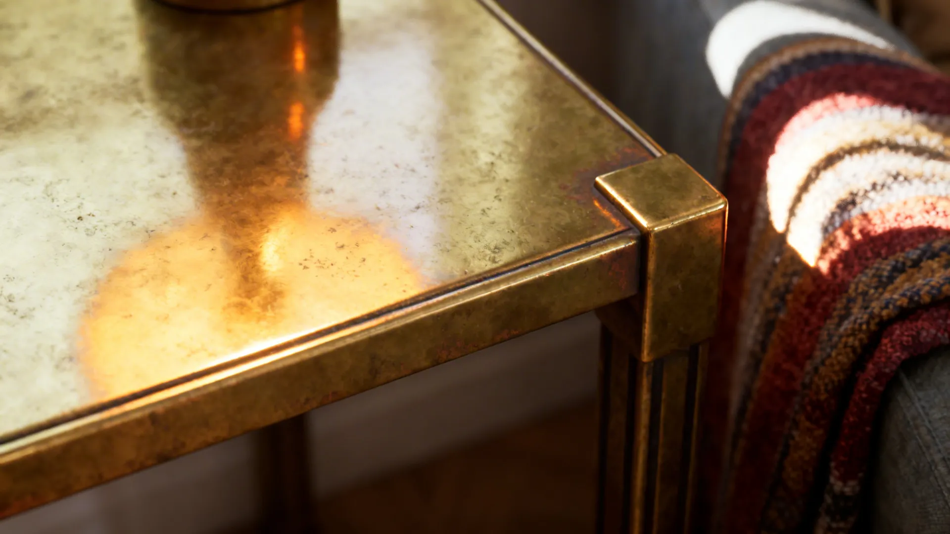 Close up of a gold metal side table corner next to a soft striped blanket