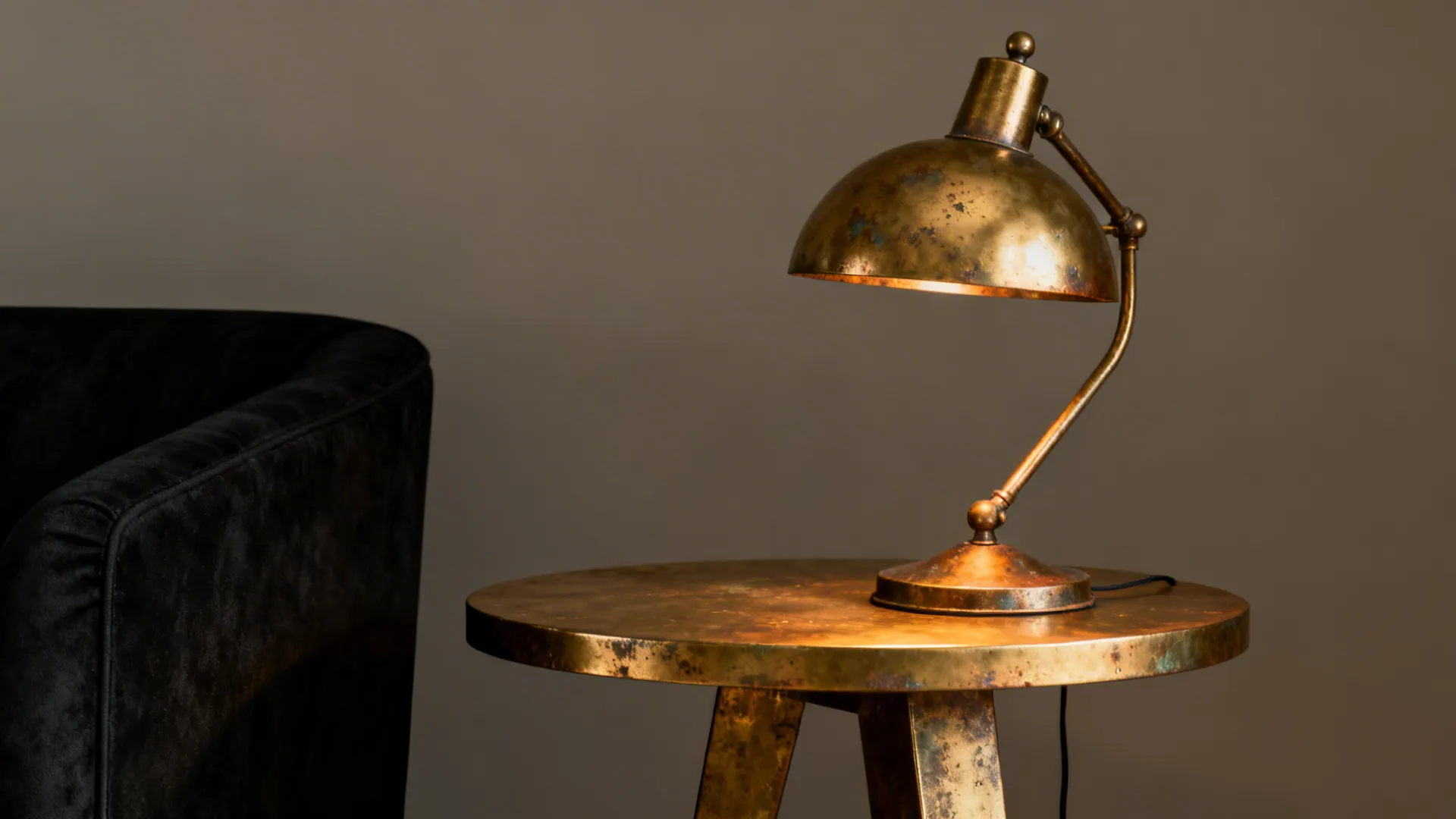 Warm brass side table and lamp beside black furniture showing patina and warm reflections.