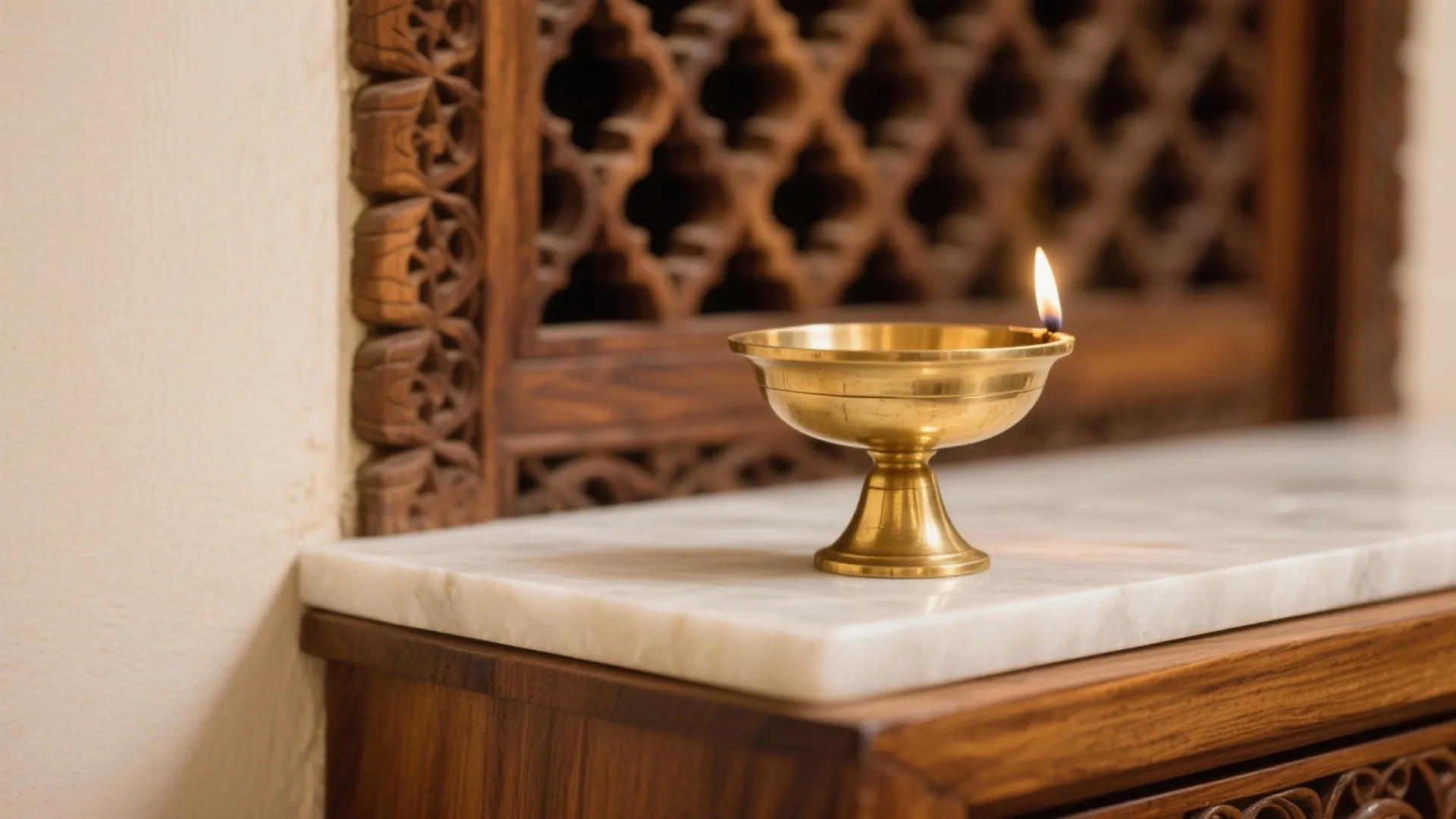 Small brass oil lamp with flame on white marble table against carved dark wood wall background