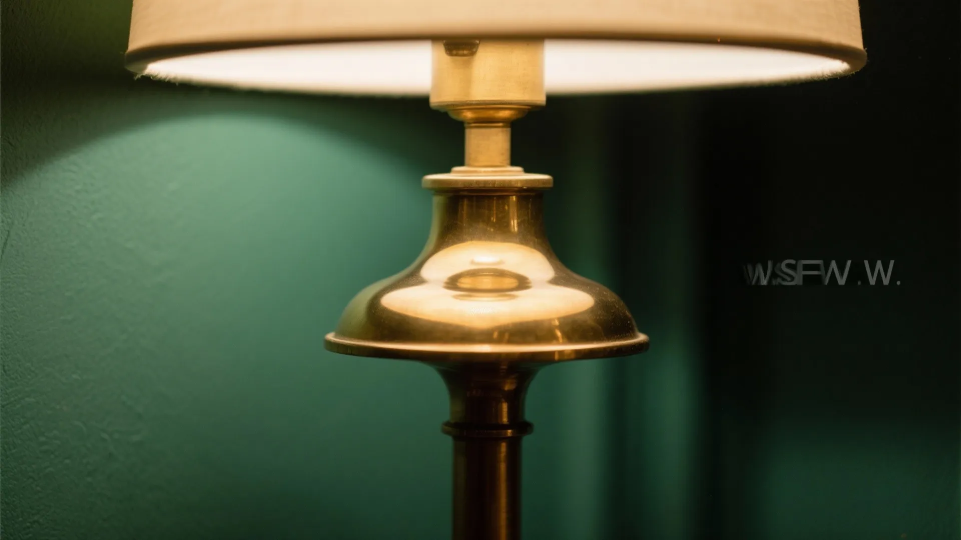Close up of a classic brass table lamp with a white shade against green wall
