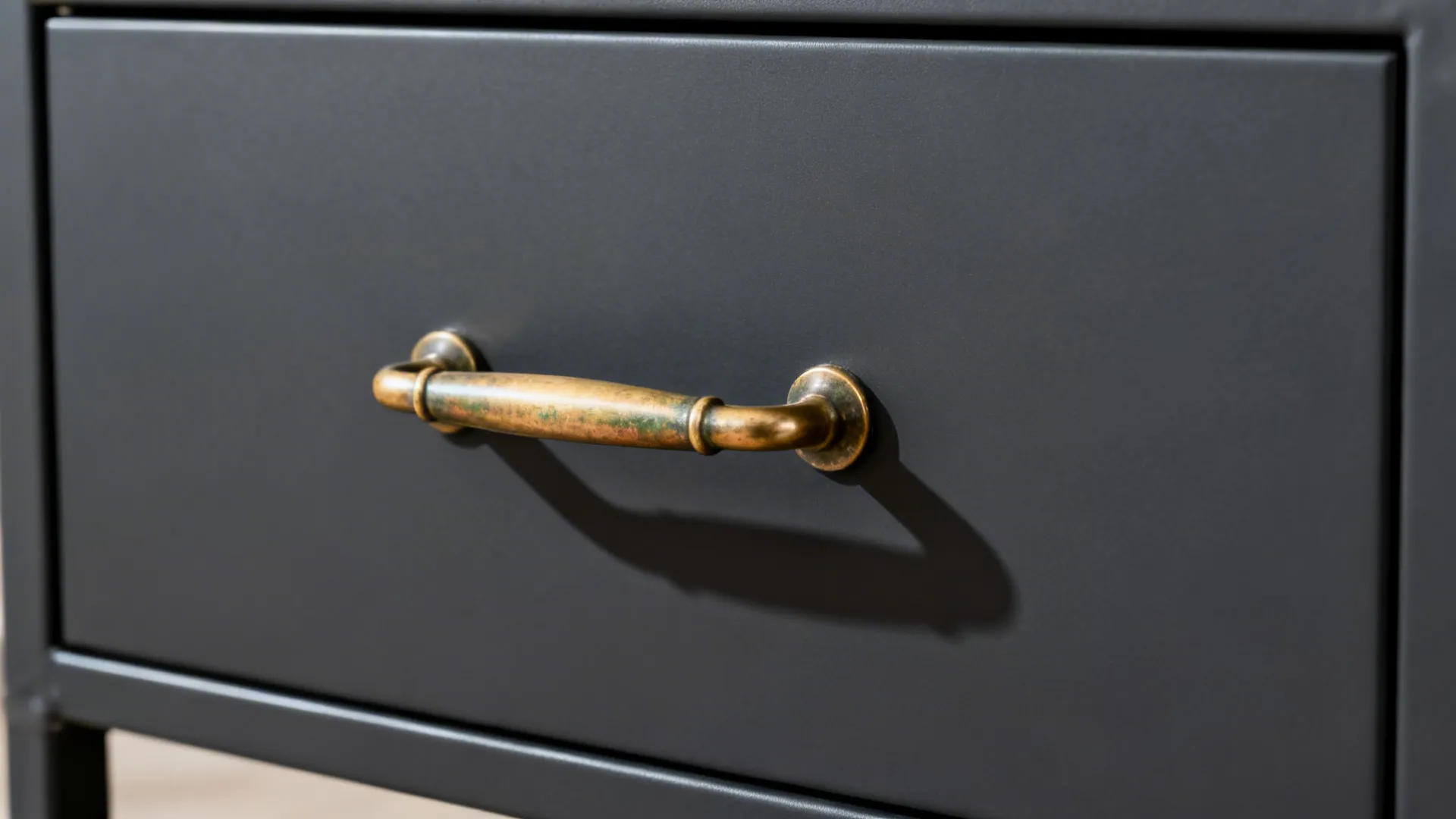 Close-up of aged brass pull on a charcoal semi-matte trolley drawer front