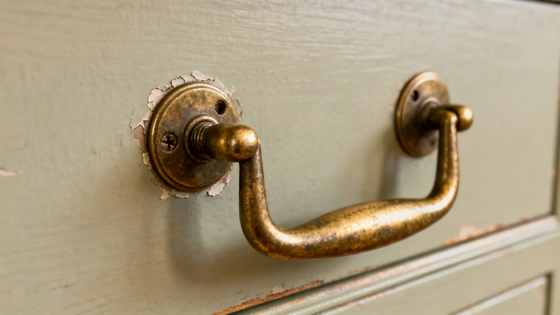 Close-up of vintage brass drawer pull on painted cabinet with subtle chipping