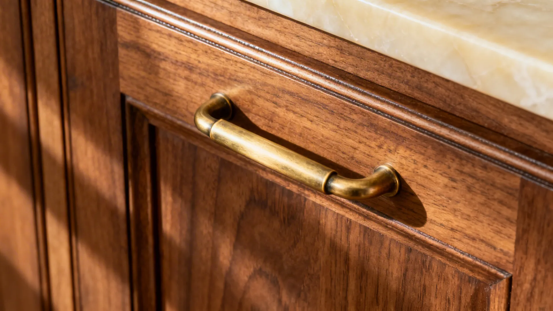 Close-up of unlacquered brass handle on warm walnut cabinet with cream quartz nearby.
