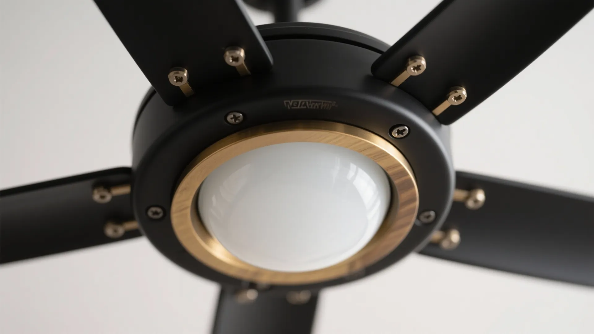 Close up of a black ceiling fan with a round white light and gold trim