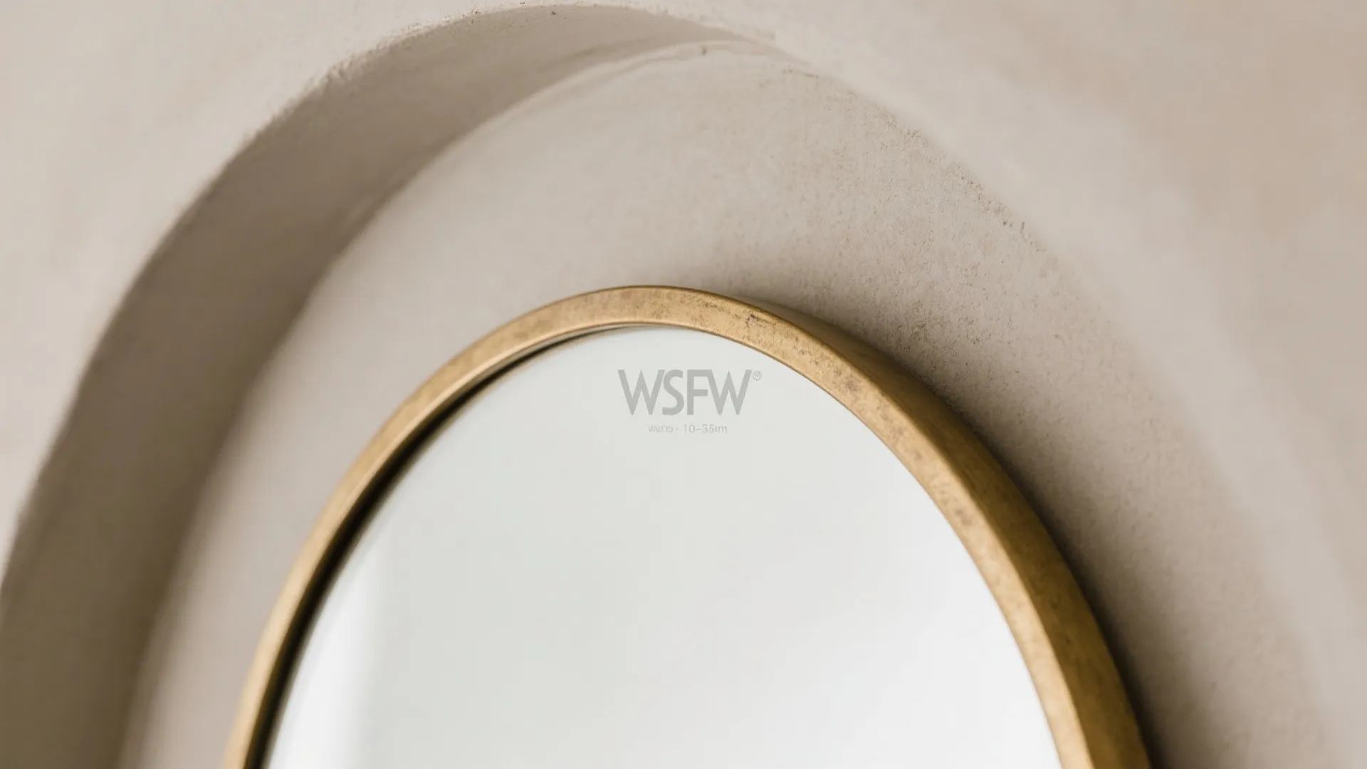 Close up view of a round wall mirror with gold frame on textured white wall