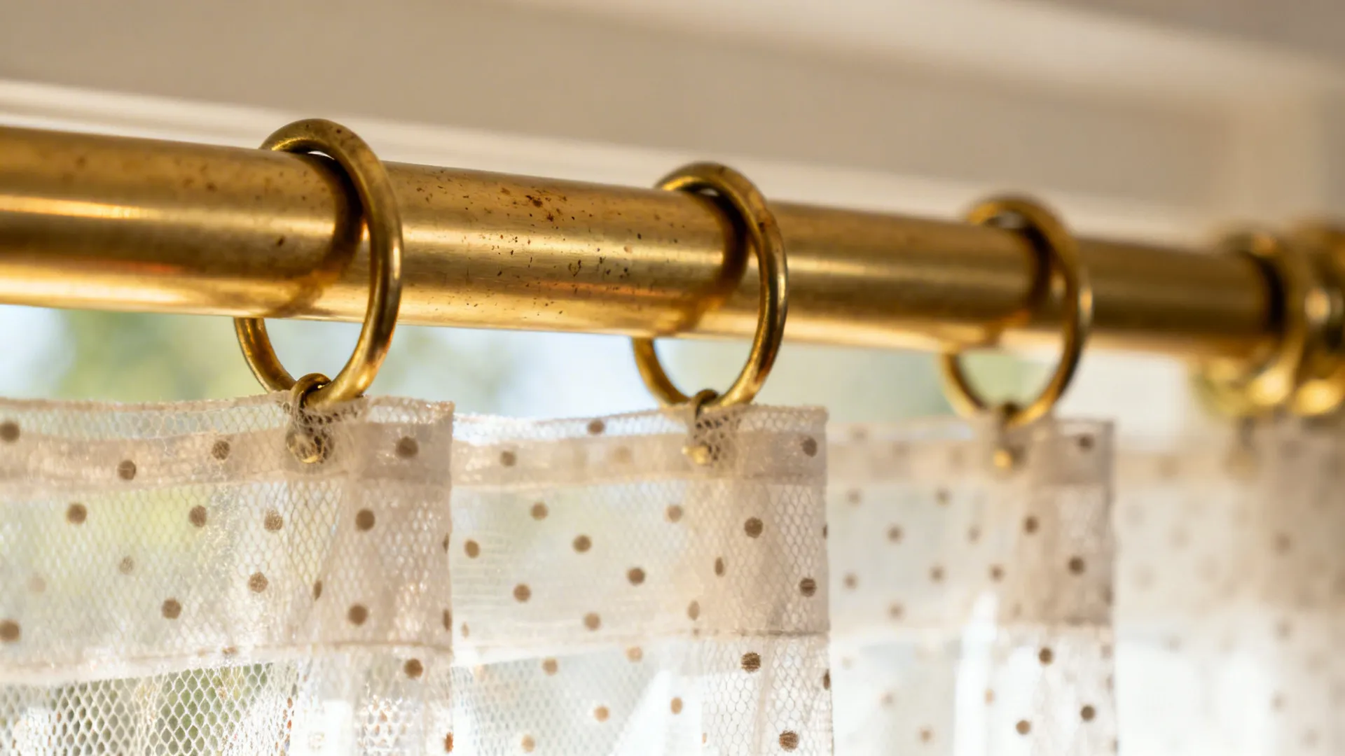Macro of an unlacquered brass café rod with a delicate net curtain showing subtle patina.