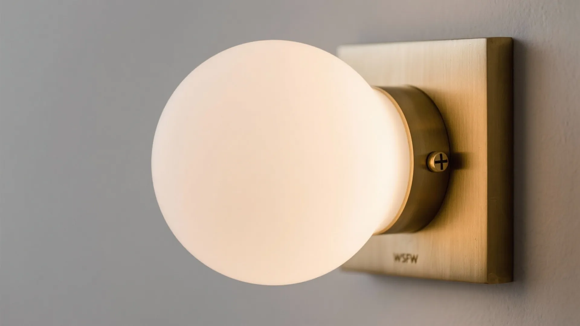 Close-up of a brass sconce with an opal diffuser showing fine brushed metal and soft light.