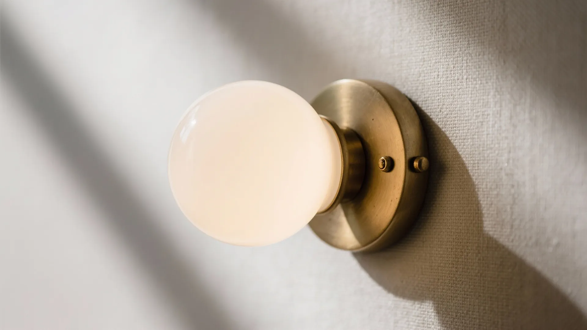 Macro of brushed brass sconce with opal glass diffuser and soft warm glow.