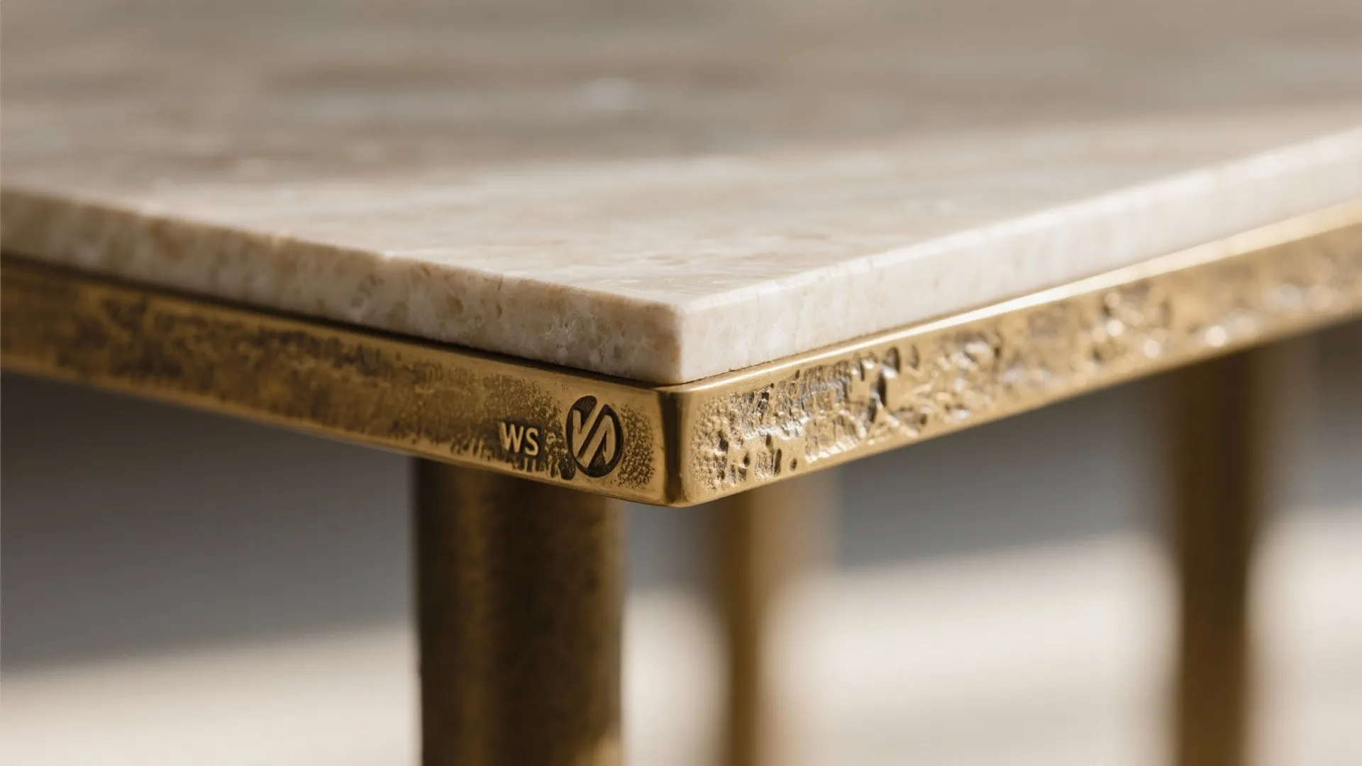 Macro of cast brass edge and honed stone tabletop with warm patina.