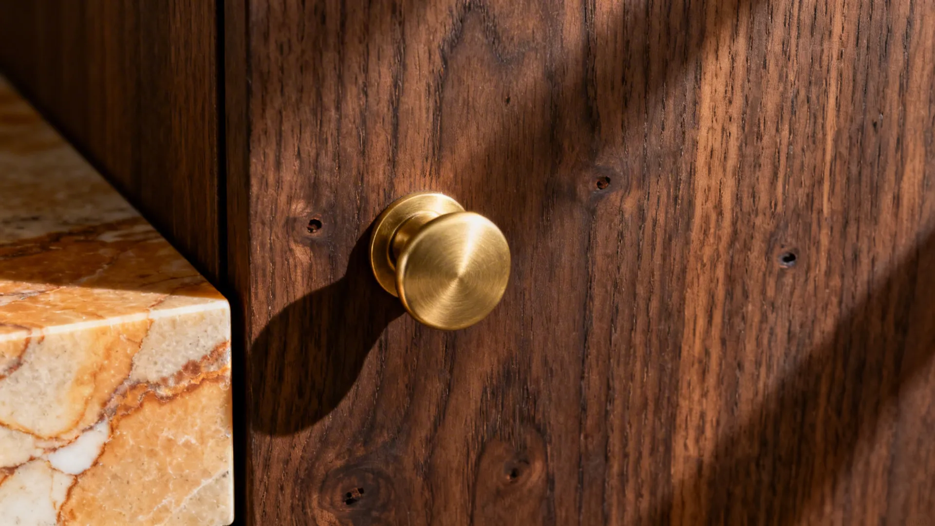Macro of brushed brass pull on walnut next to honed warm-veined quartz.