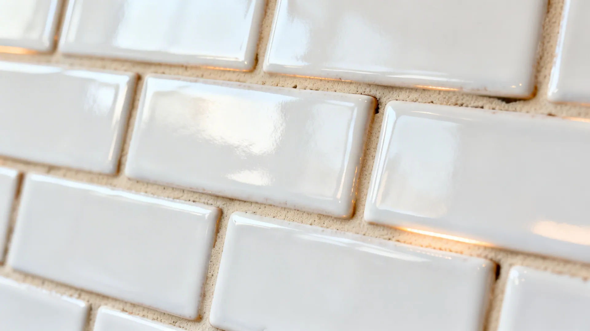 Macro of glossy white brick tiles with warm beige grout and gentle surface undulation.
