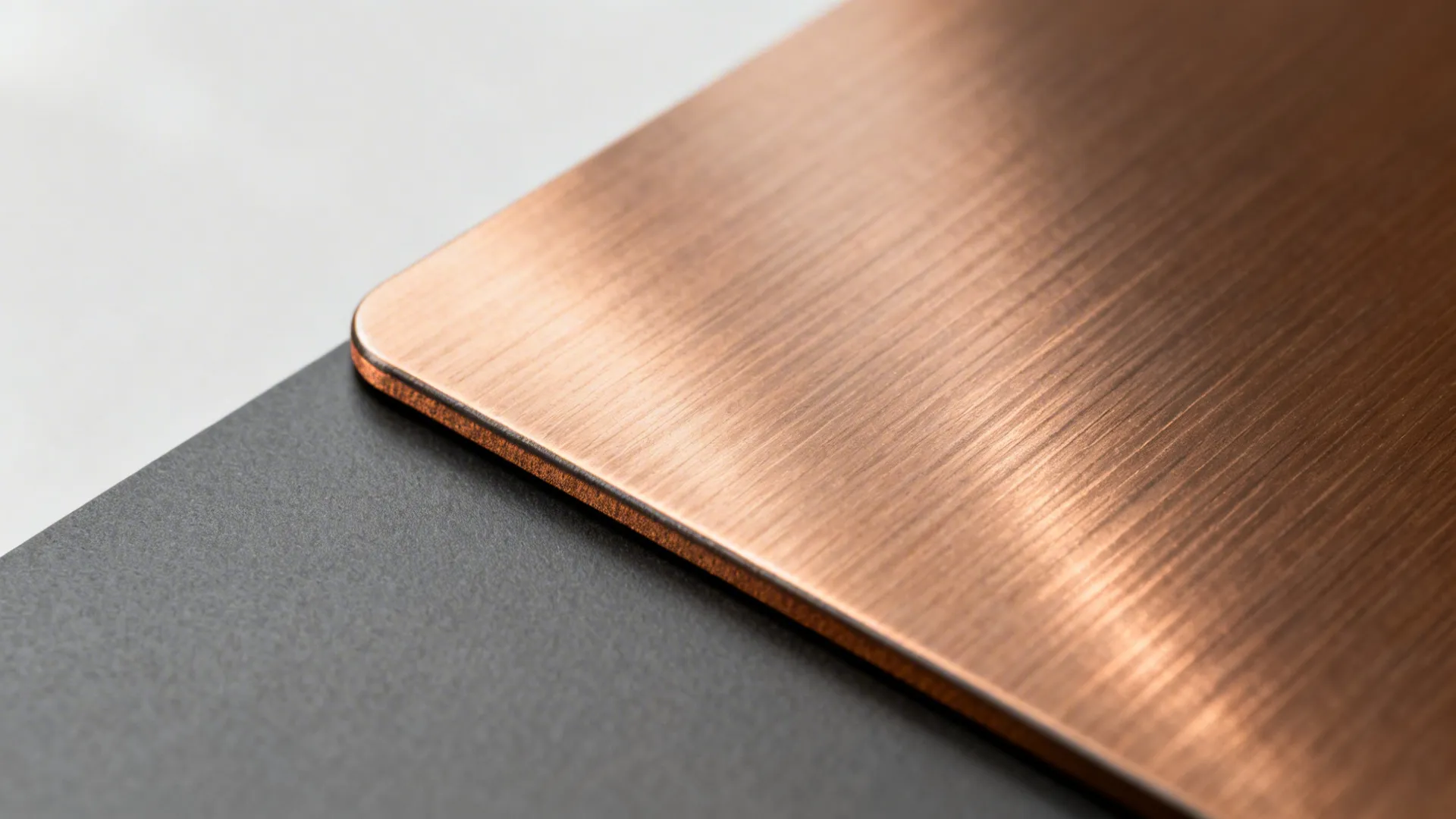 Macro of brushed bronze decolam with linear grain and soft highlights beside a matte graphite surface.