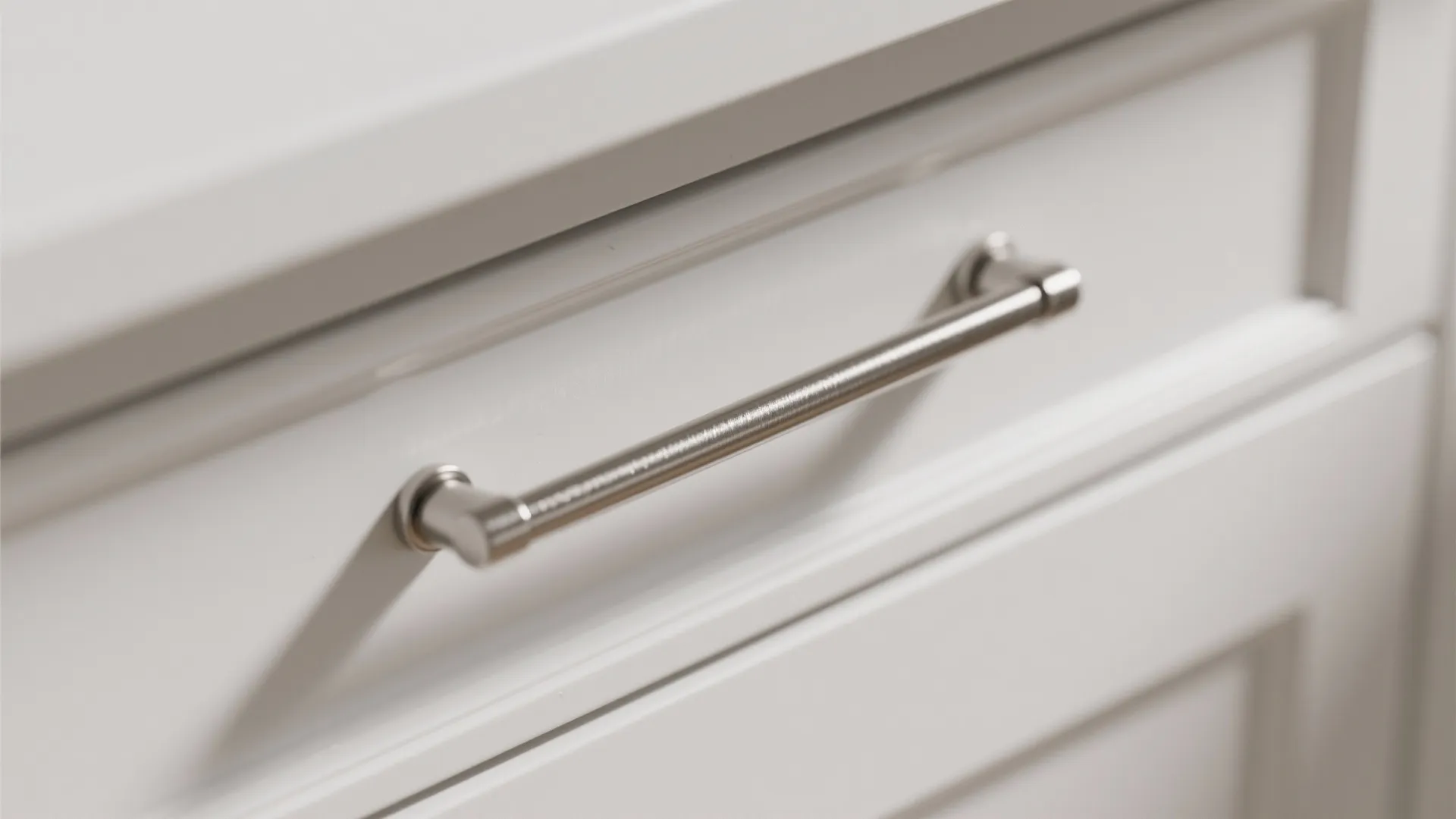 Close up of a long silver metal handle installed on a white wooden cabinet drawer