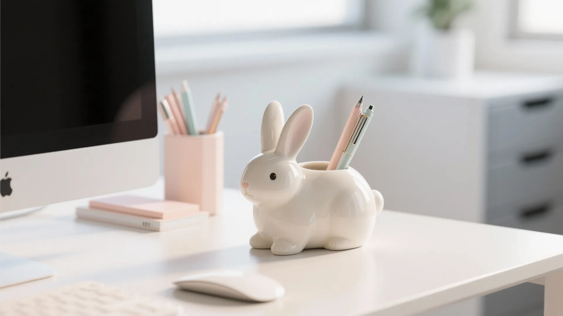 White bunny shaped pen holder on a white desk next to a computer and stationery