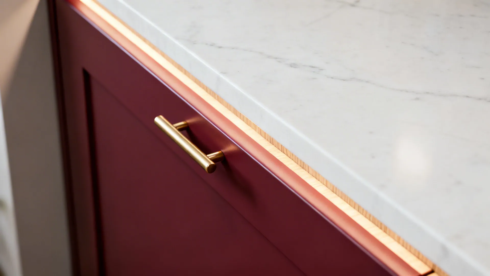 Macro of satin burgundy cabinet with brass pull against white quartz countertop.