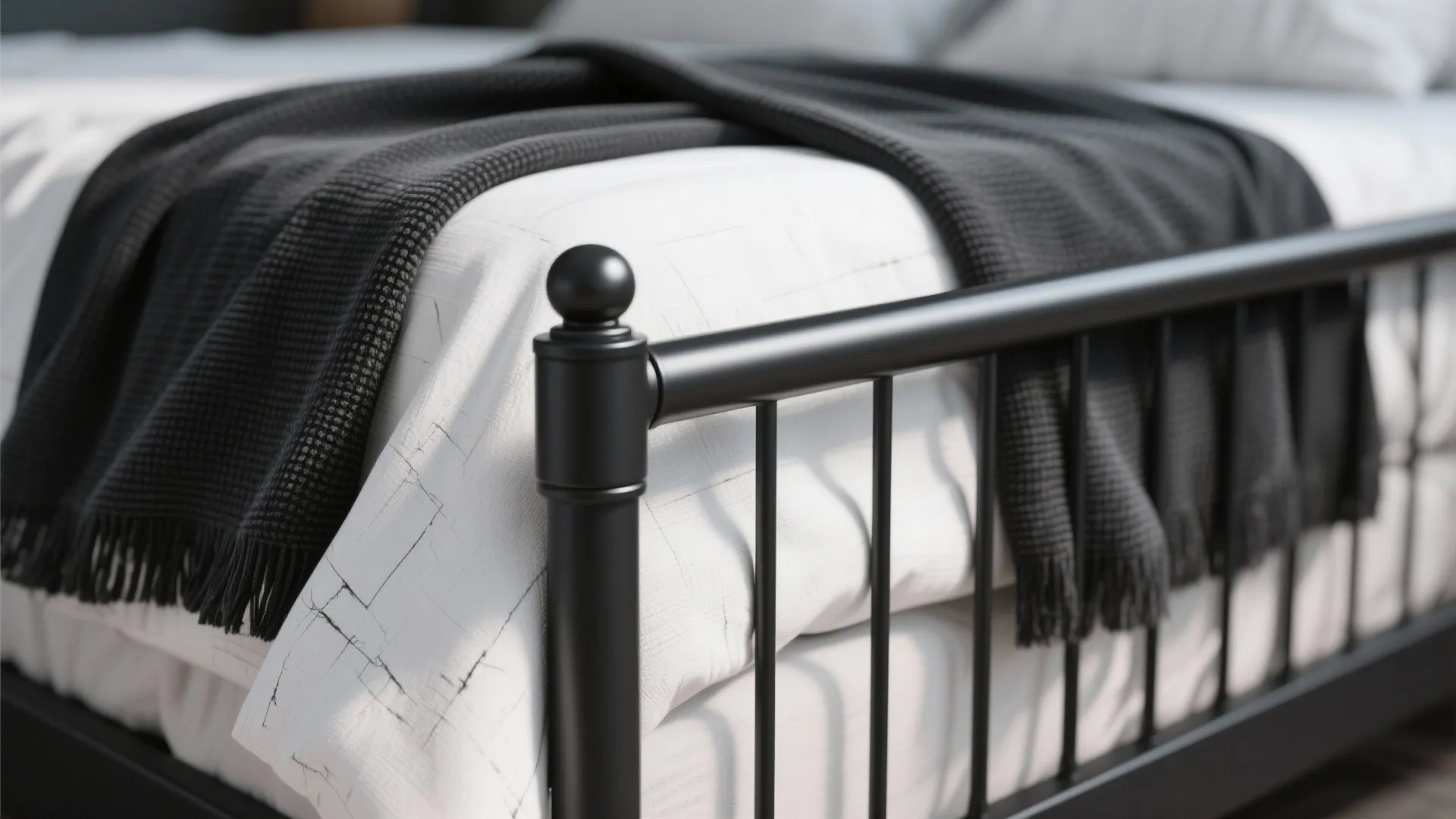 Detail of black metal bed frame featuring white sheets and a soft black knit blanket