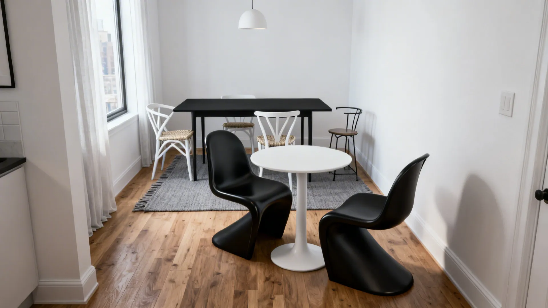 Minimalist dining area with white round table, black chairs, wooden floor, and black rectangular table