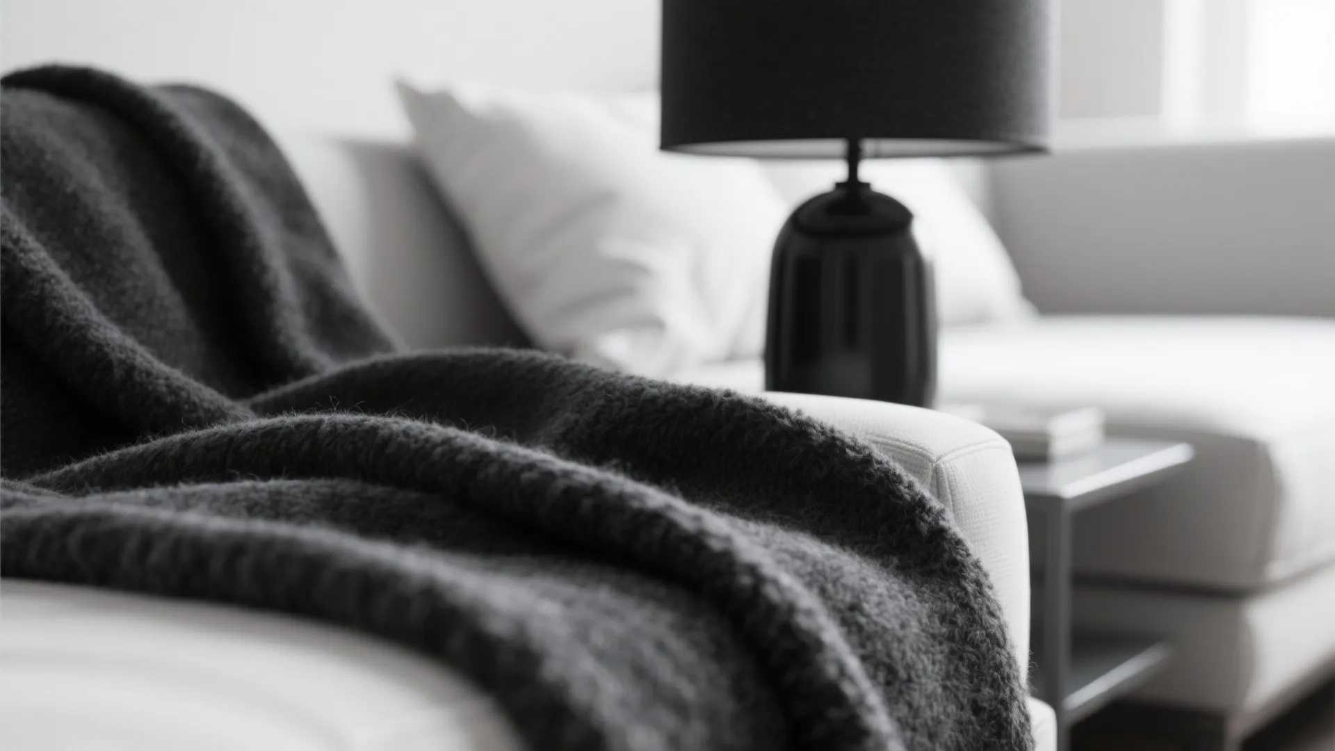 Close up of black soft blanket on white sofa with black table lamp and pillows