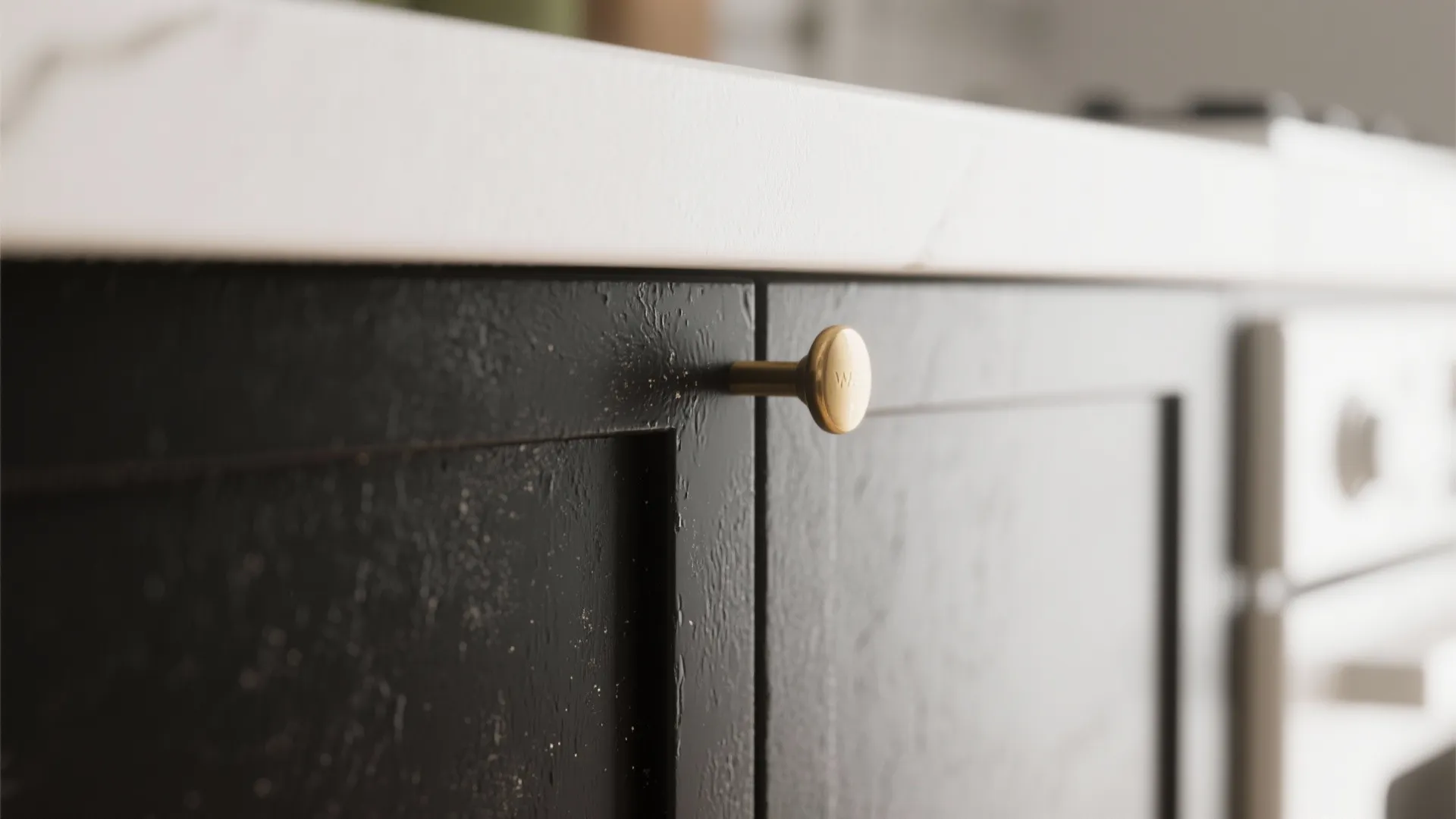 Close-up of black kitchen cabinet doors featuring a gold round handle and smooth white countertop