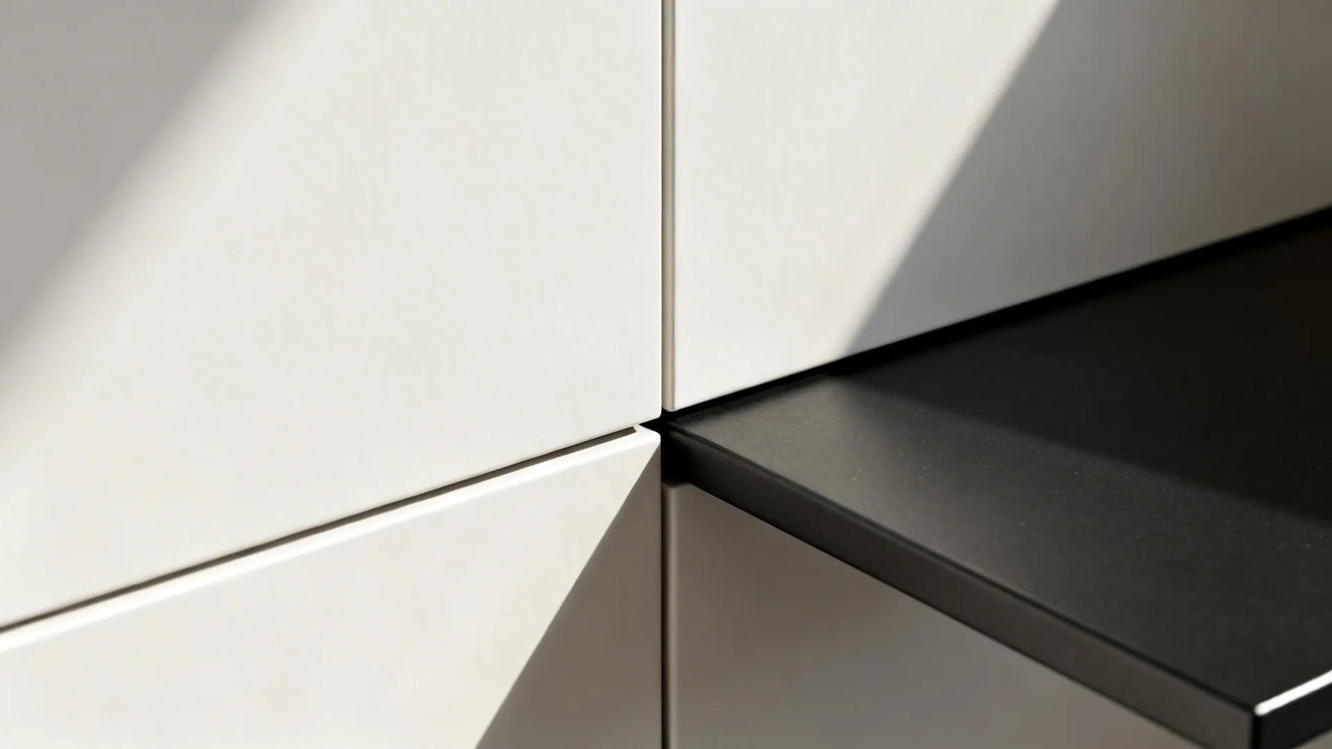 Macro detail of matte white handleless cabinets and a black steel shelf with crisp shadow lines.