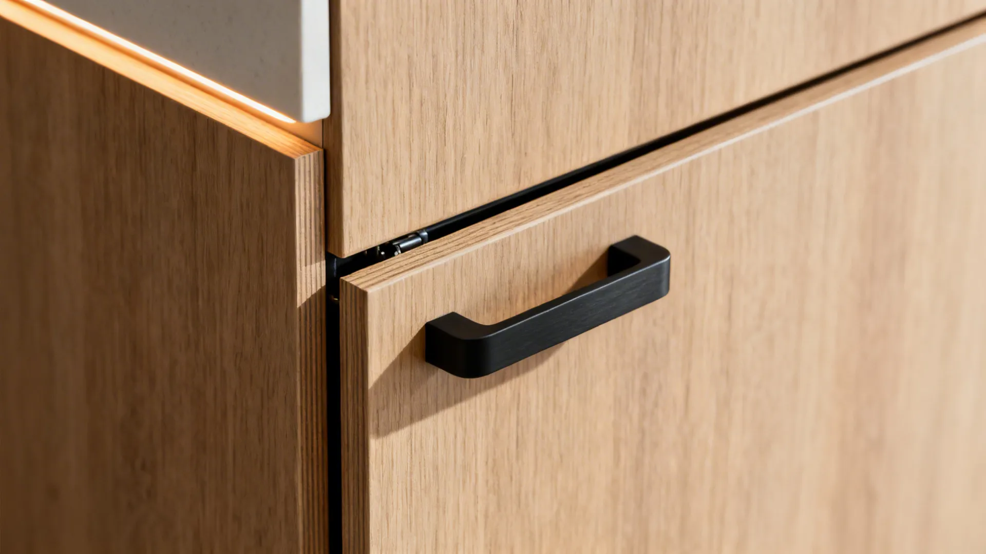 Close-up of a black metal handle on a light wood cabinet with warm under lighting