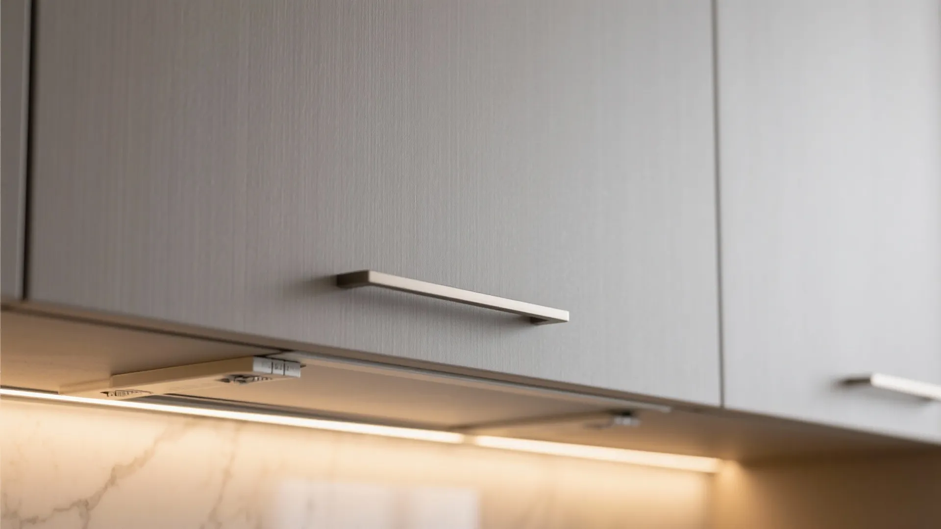 Gray kitchen cabinet doors with slim metal handles and a warm light fixture glowing underneath