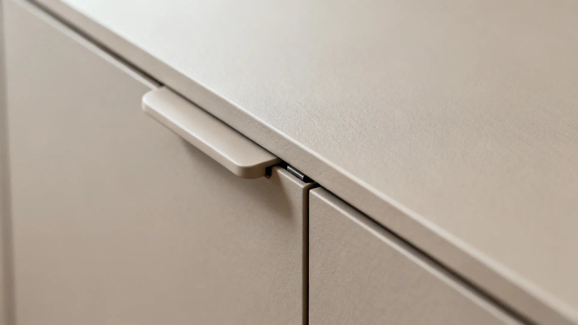 Macro of matte beige cabinet door with integrated pull and push-to-open detail in a studio kitchen.