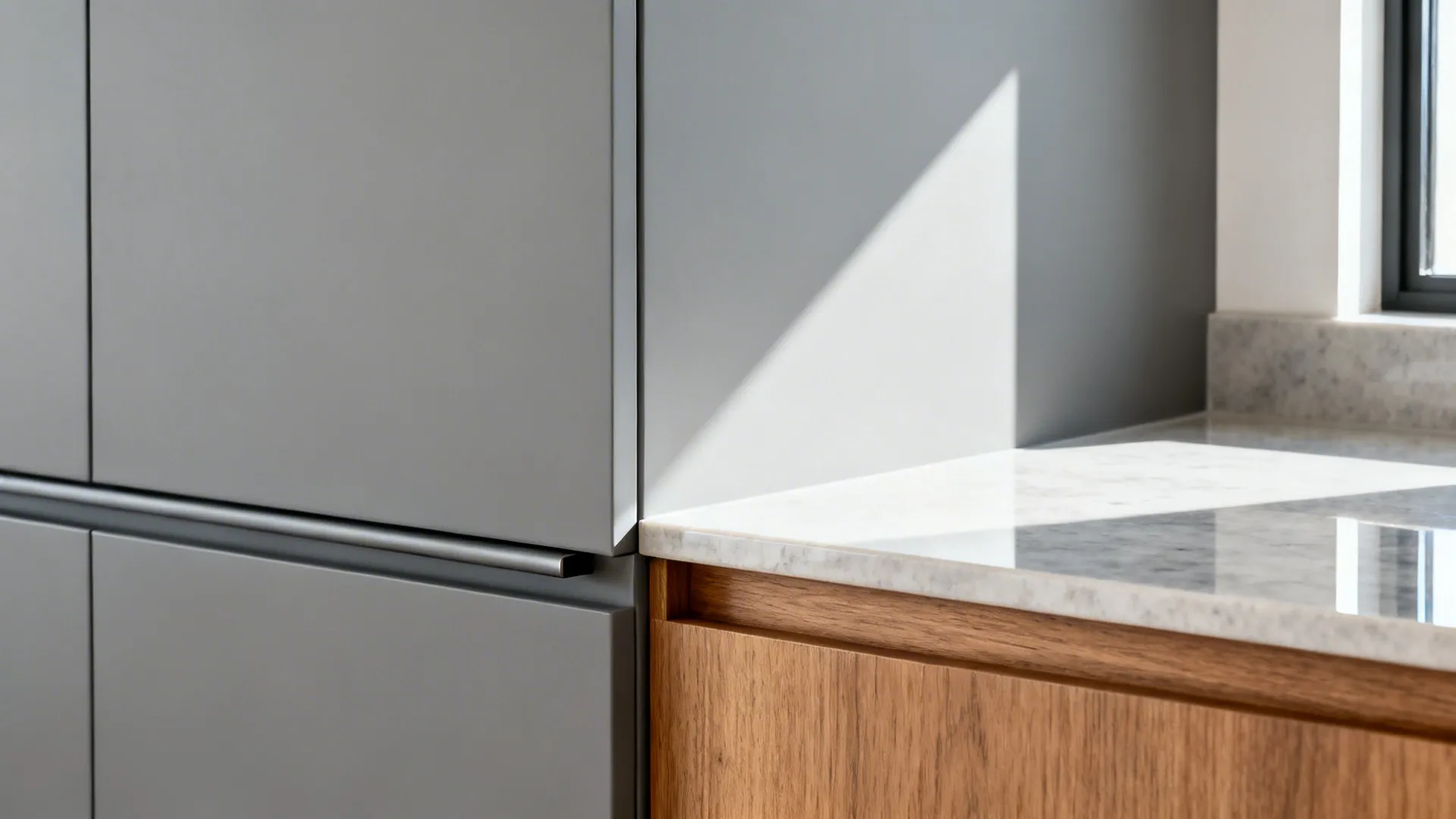 Macro of integrated pull rail on matte gray tall cabinet meeting warm wood base unit with quartz countertop.