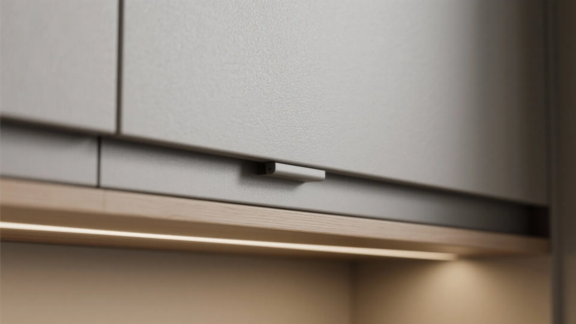 Close up of grey kitchen cabinet door with simple handle and warm light fixture strip underneath