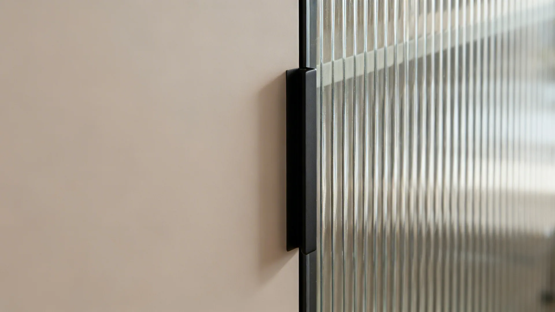 Macro detail of matte cabinet door meeting ribbed glass with slim black hardware.