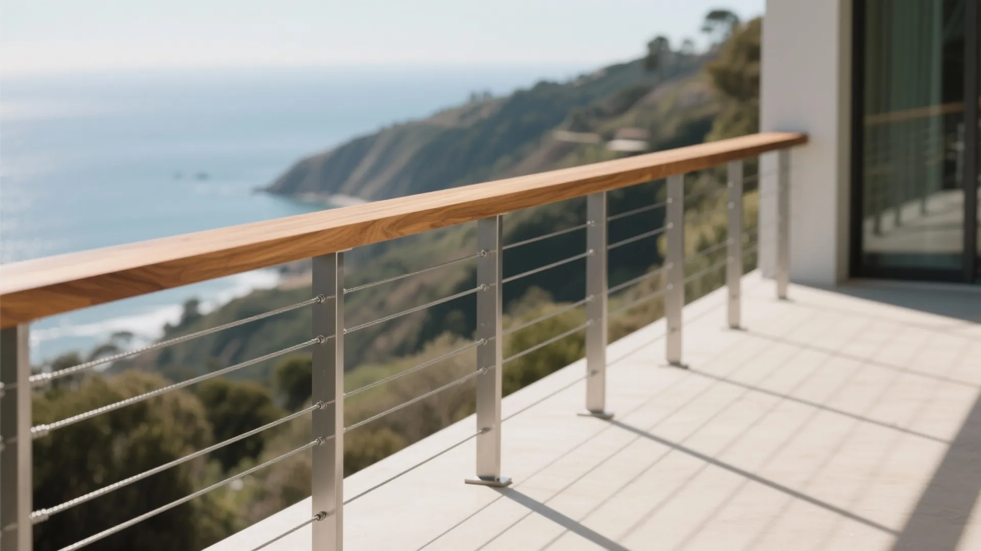 Outdoor terrace with wood handrail and metal cable railing overlooking the blue ocean and hills