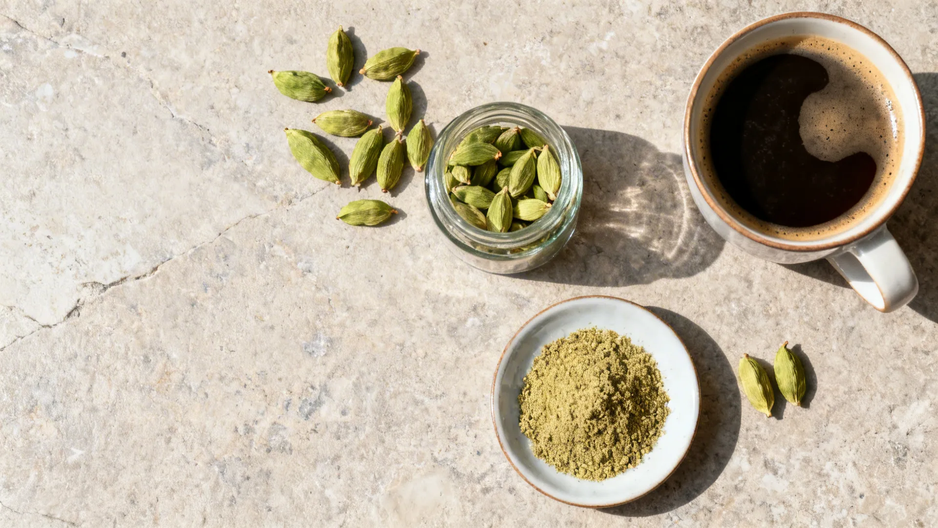 Flat lay with green cardamom pods, ground cardamom, a storage jar, and a coffee cup.