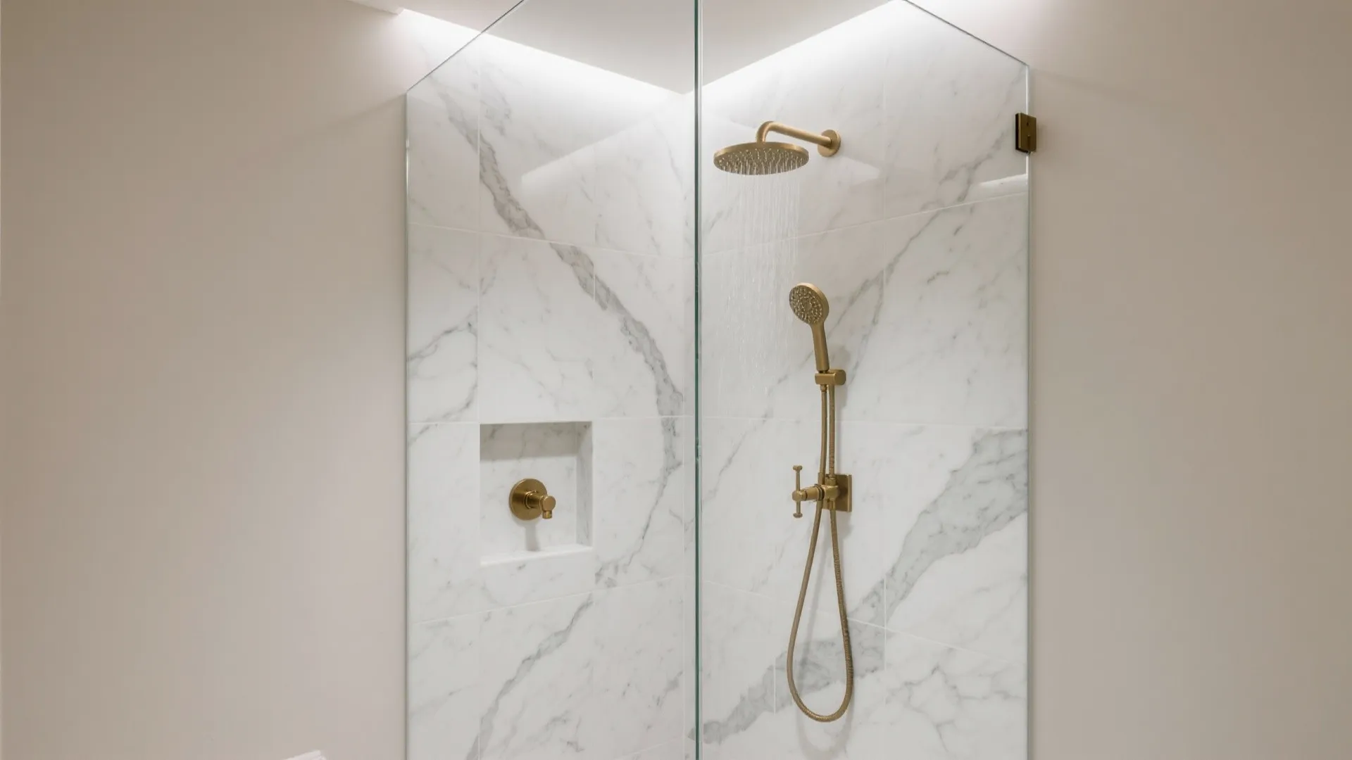 Modern shower area featuring white marble wall tiles, gold shower head, and glass door partition