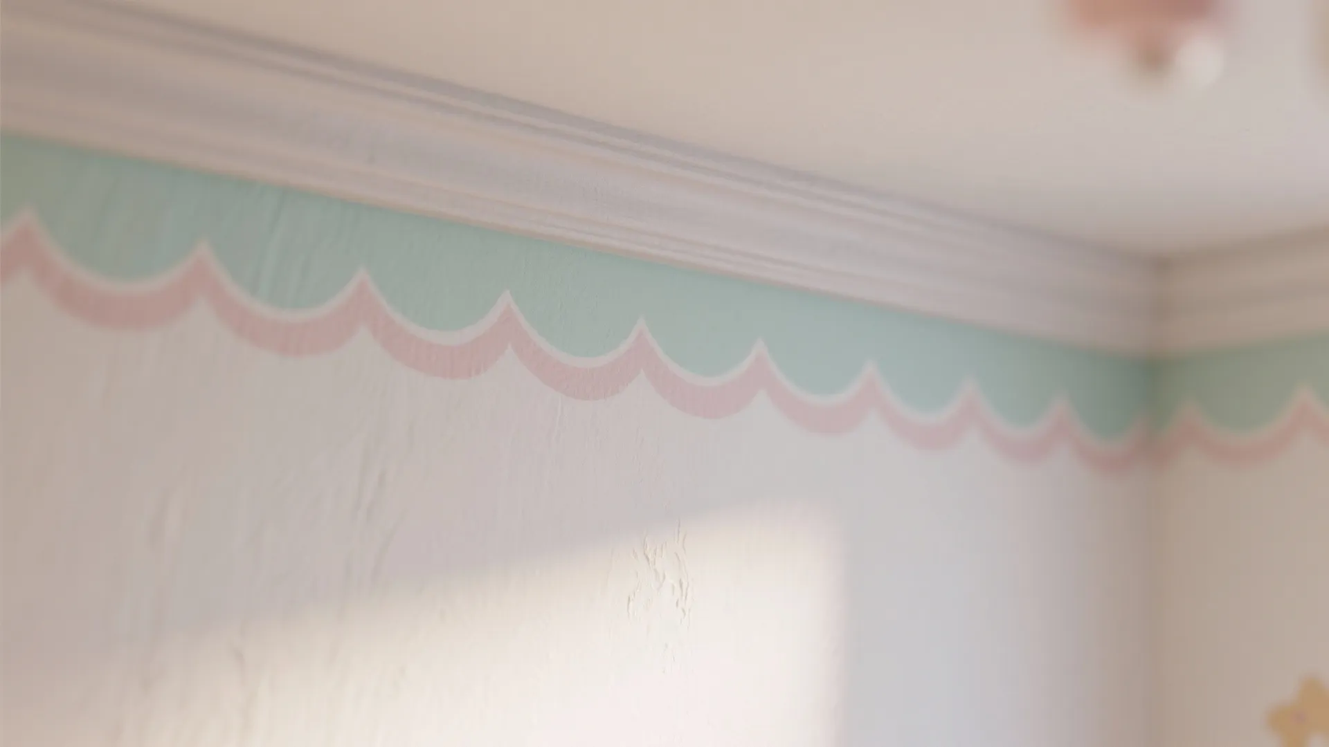 Close up of white wall featuring a pink and mint green wavy pattern near ceiling