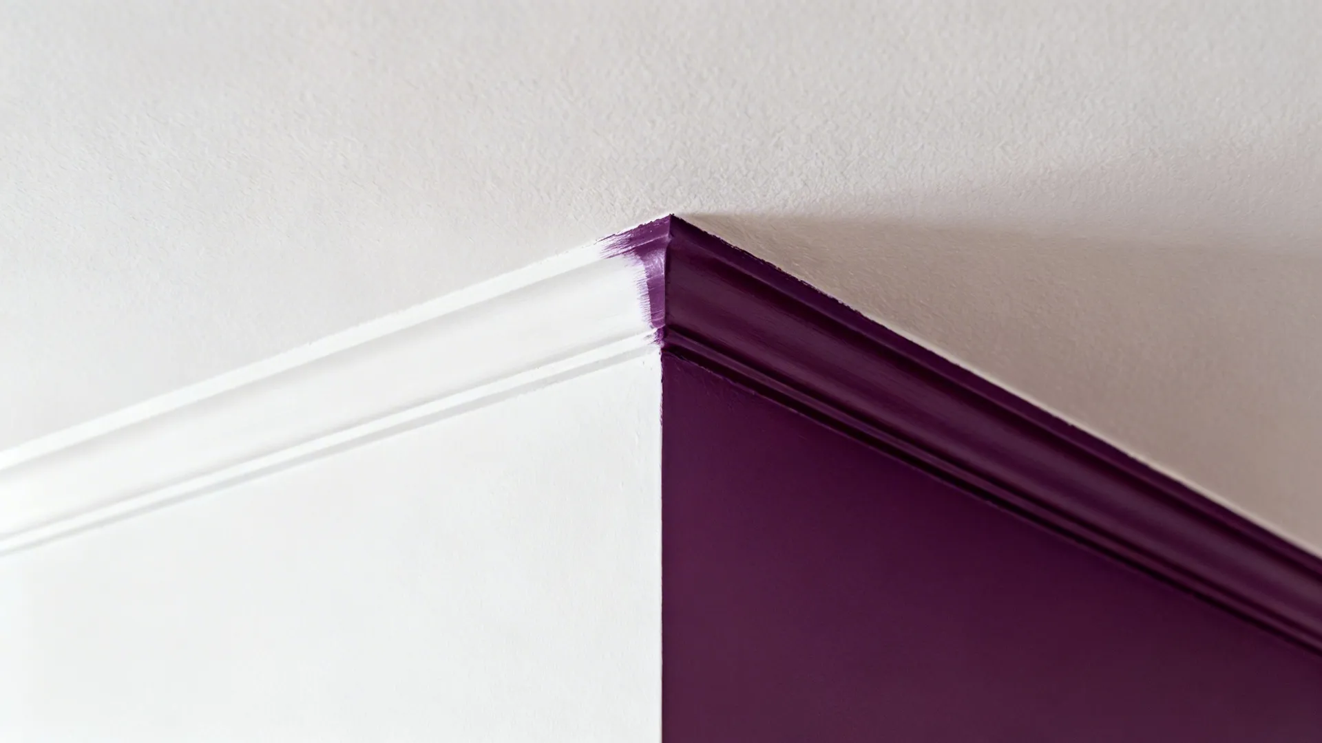 Close-up of a clean paint line between white wall and aubergine ceiling under warm light.