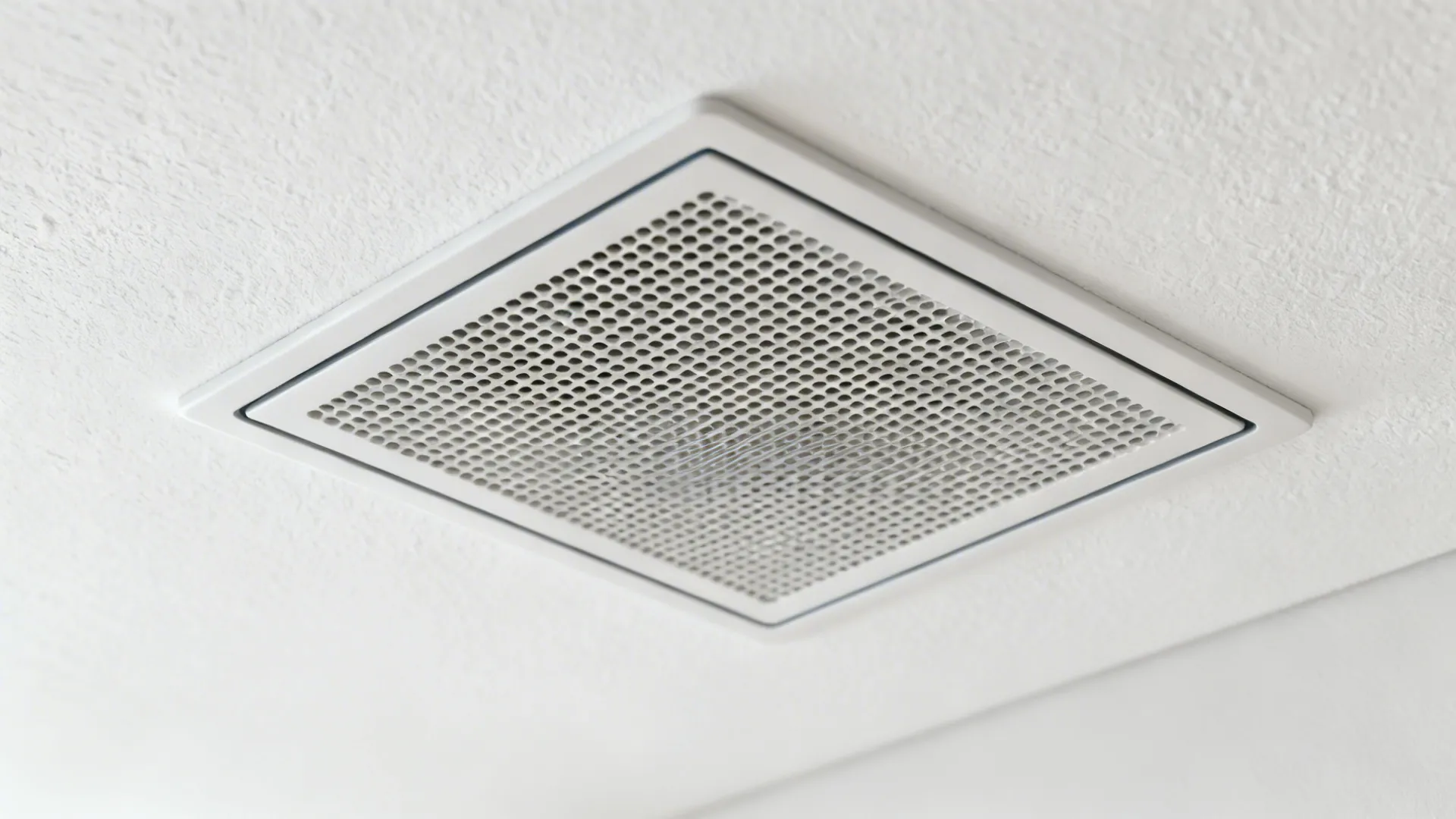 Macro detail of a flush ceiling exhaust grille set into a white painted ceiling.