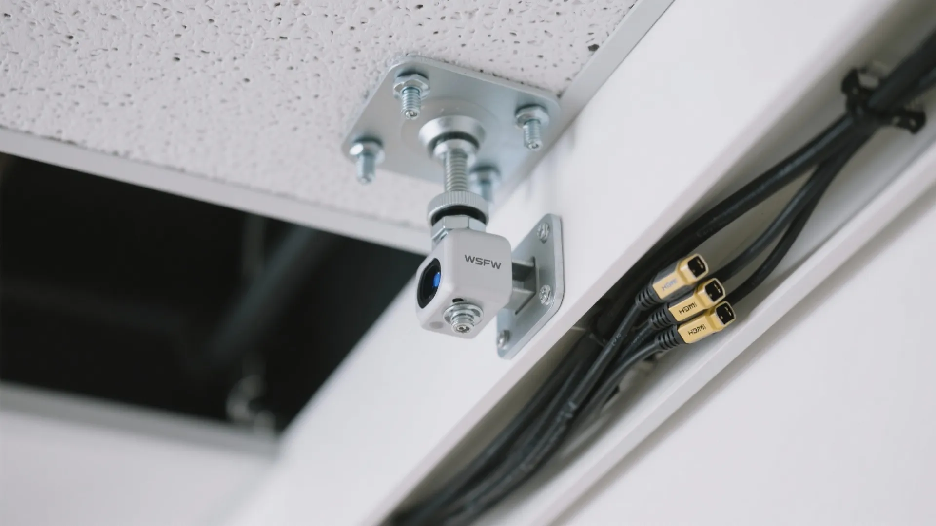 Close up of a small white camera mounted on a ceiling with several black cables