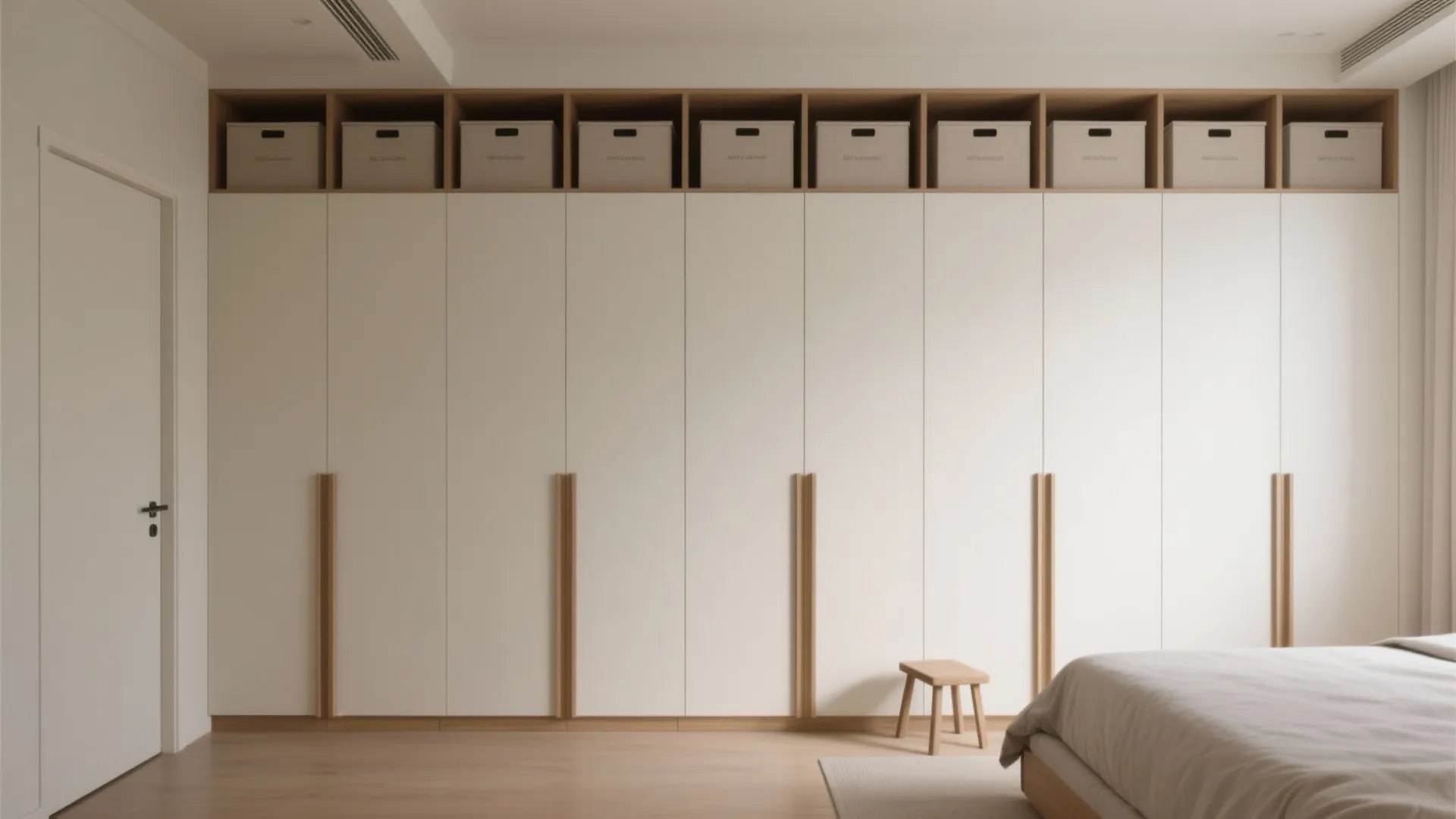 Minimalist bedroom featuring floor to ceiling white cabinet with top storage boxes and wooden stool