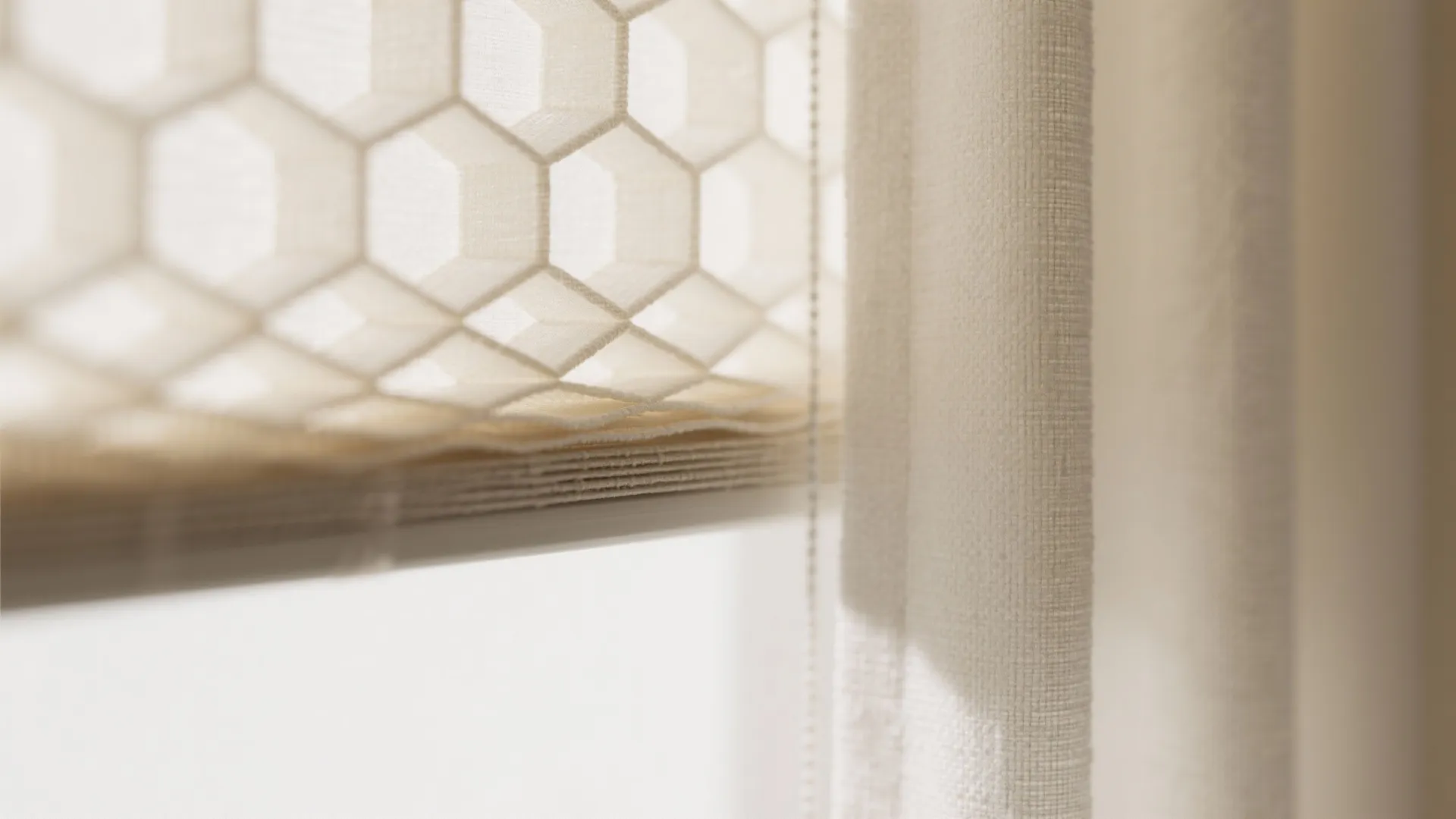 Close up of cream window blinds with honeycomb pattern next to a soft white curtain