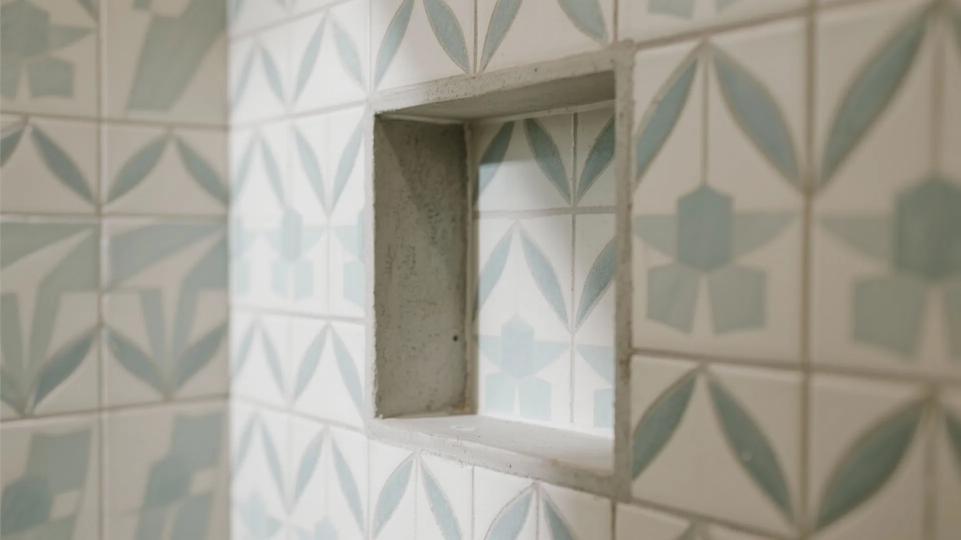 Close-up of a shower niche with soft geometric cement-look porcelain tiles in muted coastal tones.