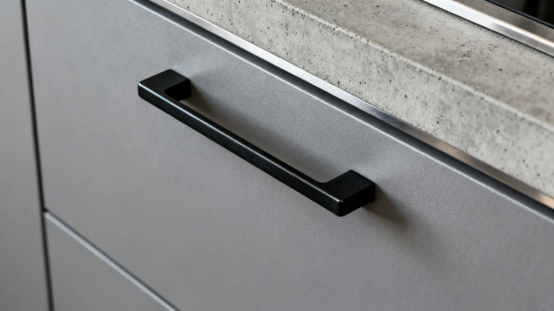 Macro of satin cement grey cabinet with black pull and concrete-look tile.
