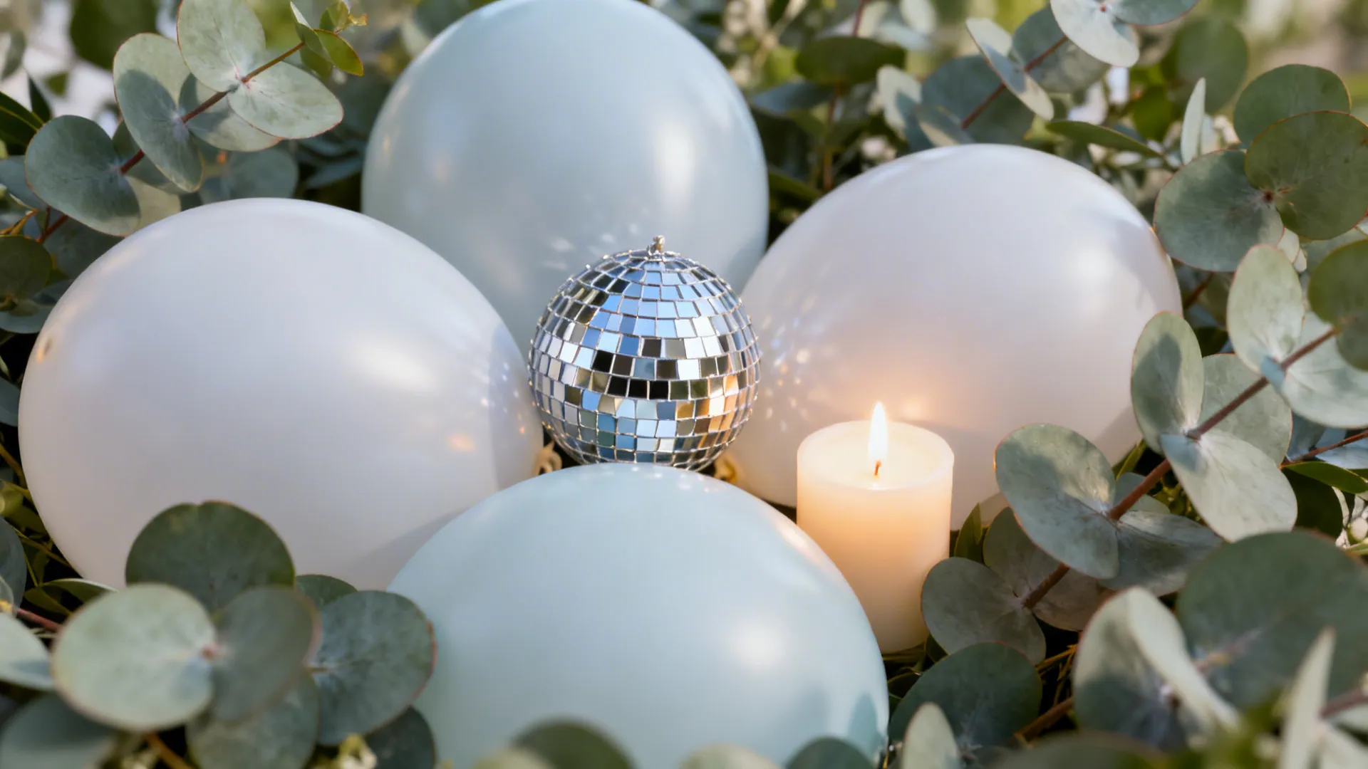 Centerpiece decoration with white balloons green plant leaves a small disco ball and one candle